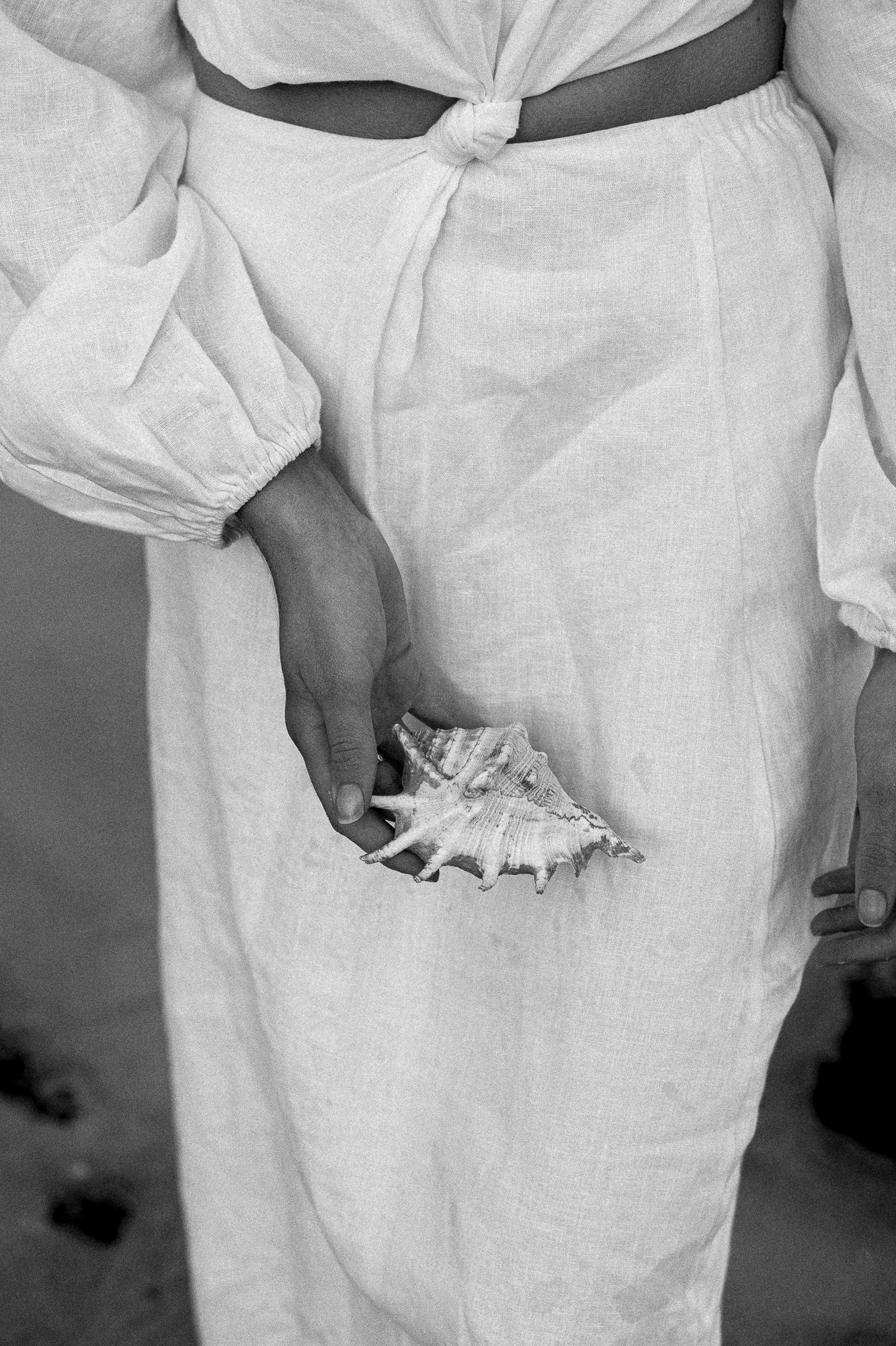 Person wearing light-colored clothing holding a large seashell in their hand.