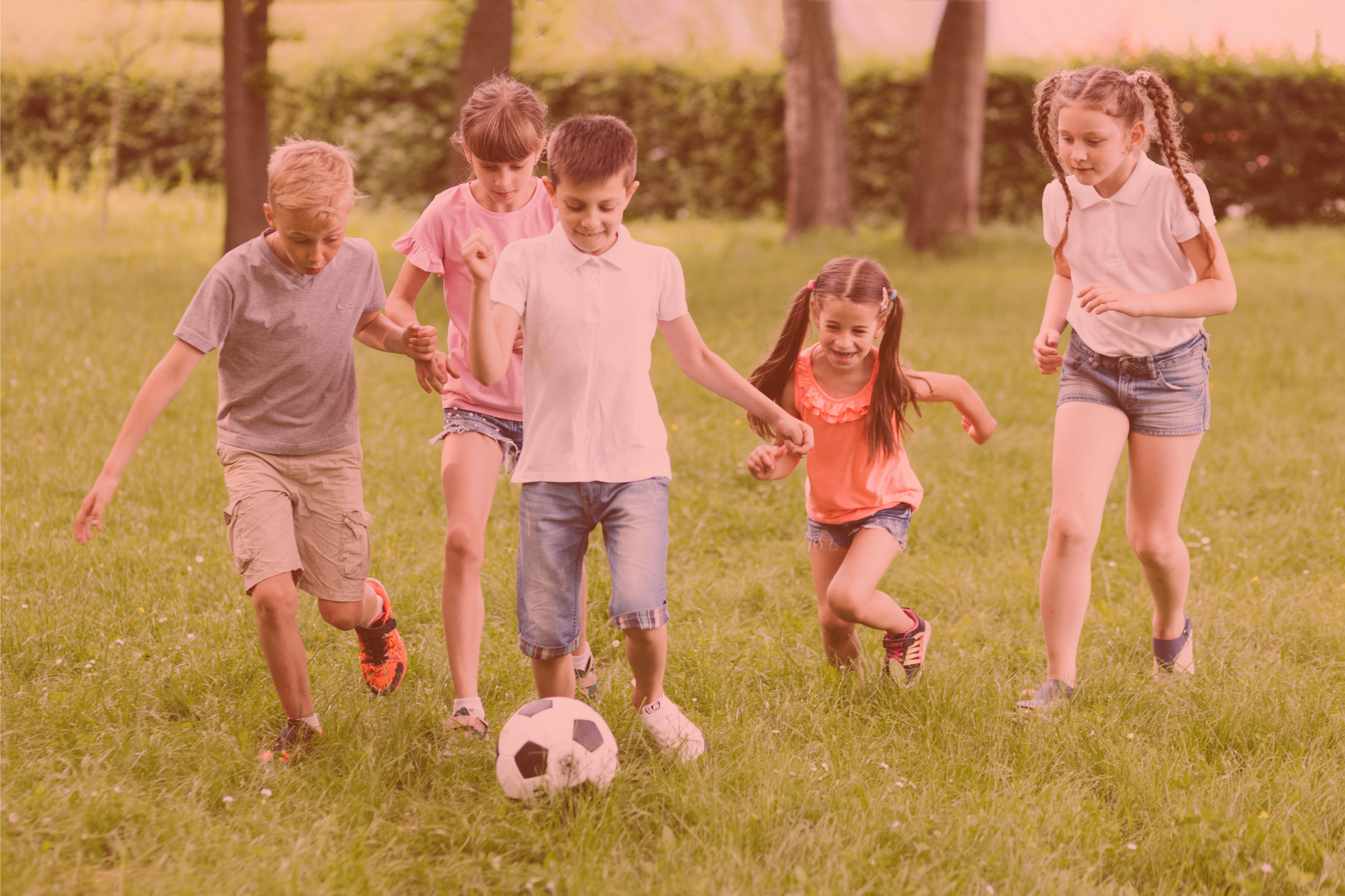 Group of happy children playing soccer together in a sunny green park.