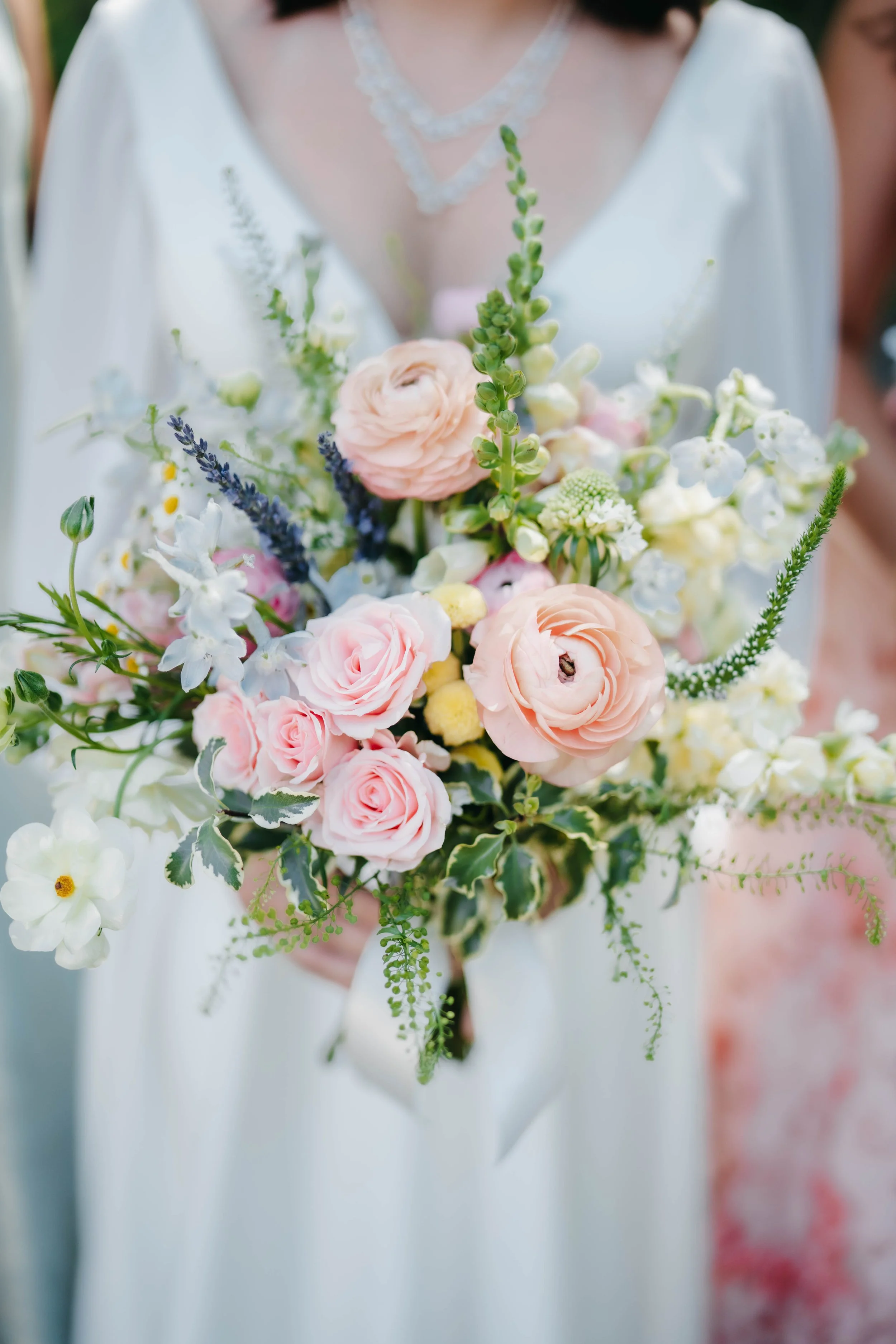 A woman in a white dress holds a bouquet of pink, white, and green flowers with various greenery.