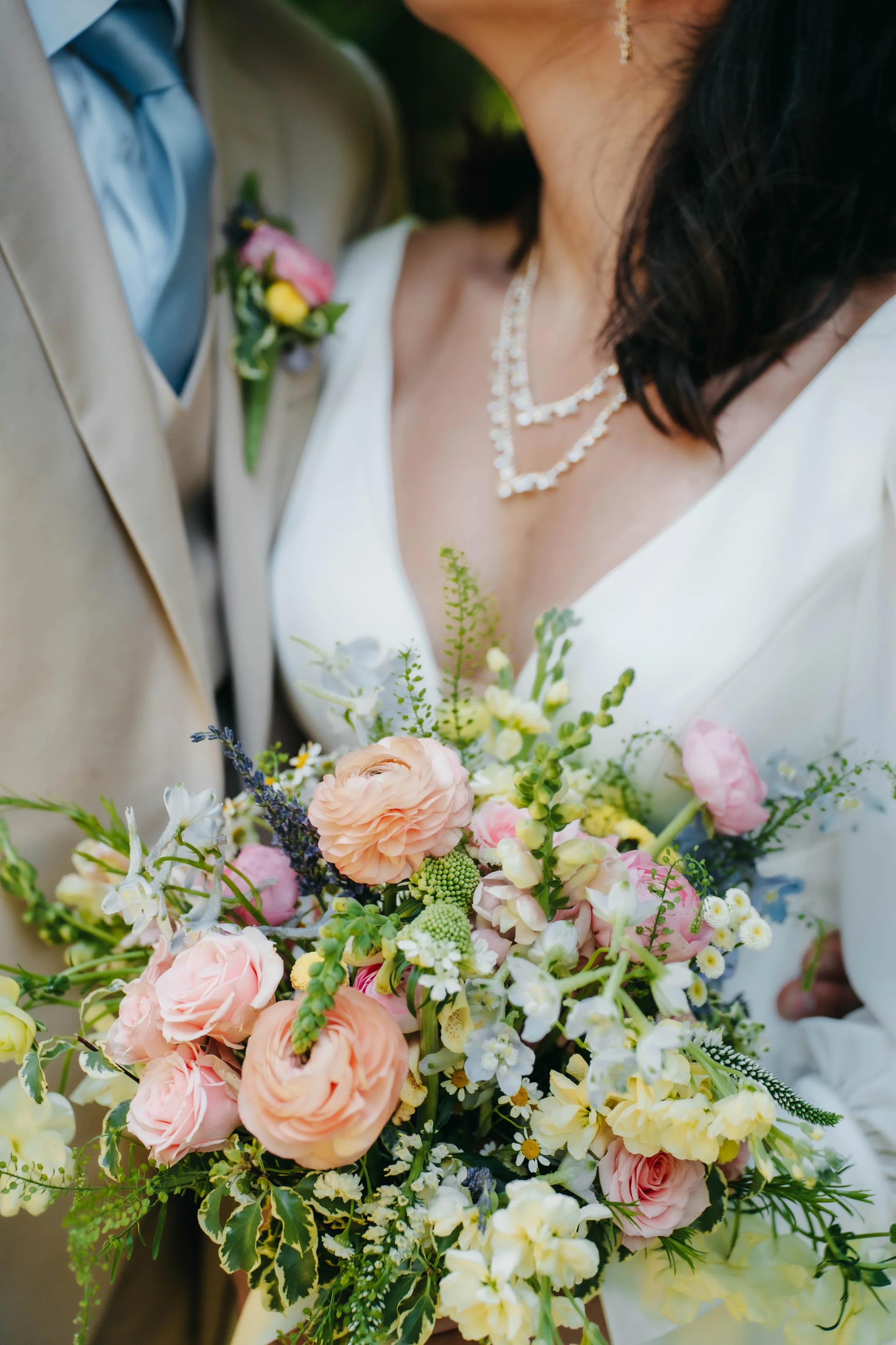 Close-up of a bride and groom holding a bouquet of pink, white, and yellow flowers during their wedding.