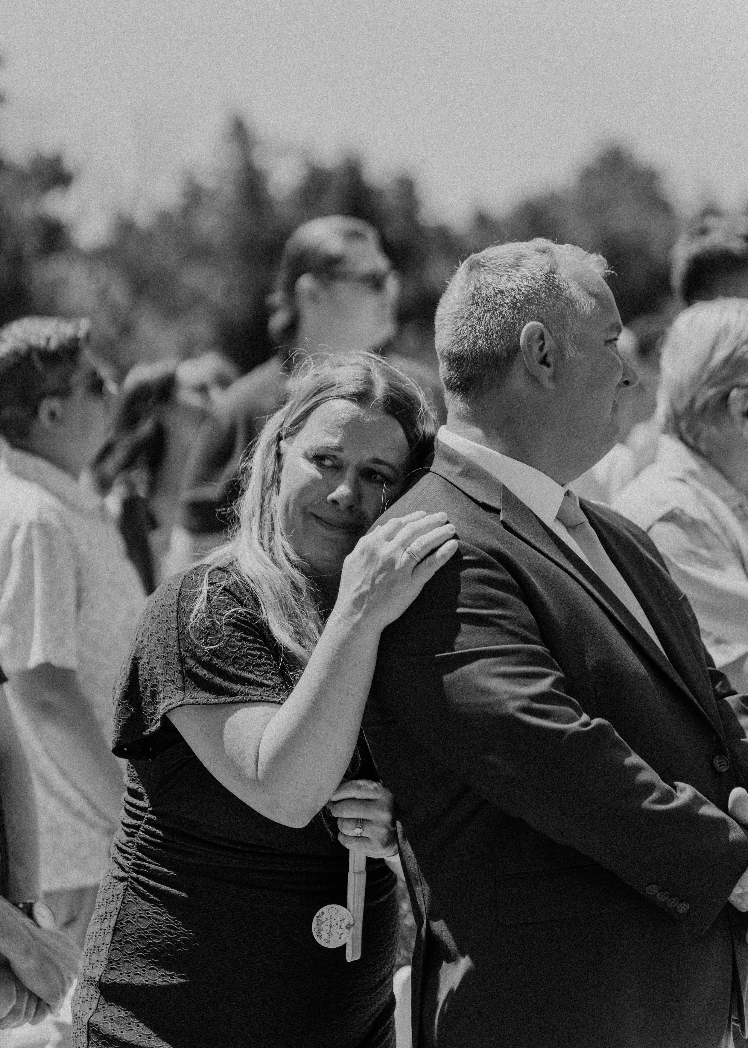 A woman is emotional and appears to be crying while embracing a man at an outdoor gathering, with several other people standing nearby.