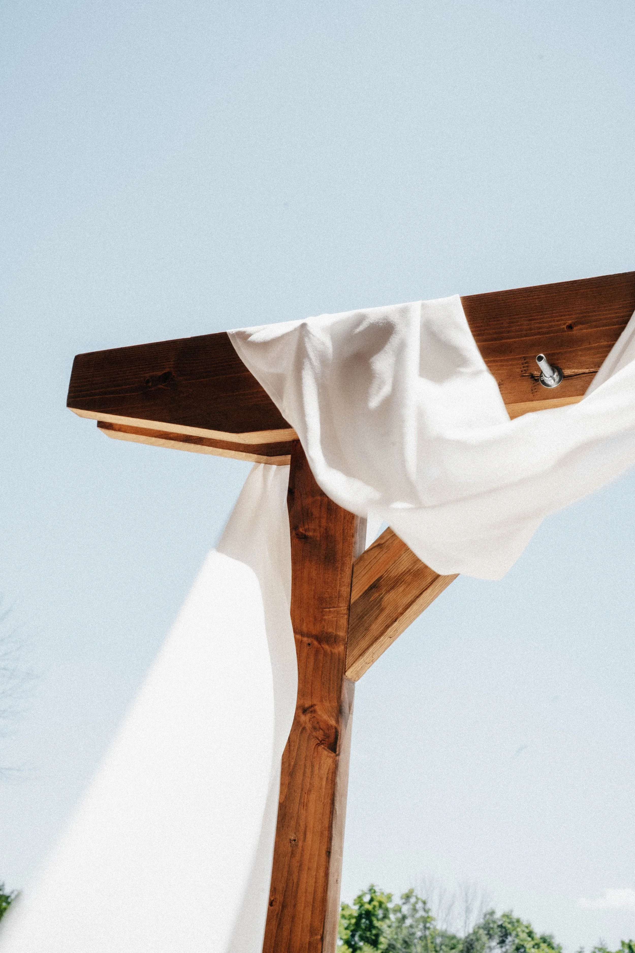 Close-up of a wooden structure with a white cloth draped over it, against a clear blue sky with trees in the background.