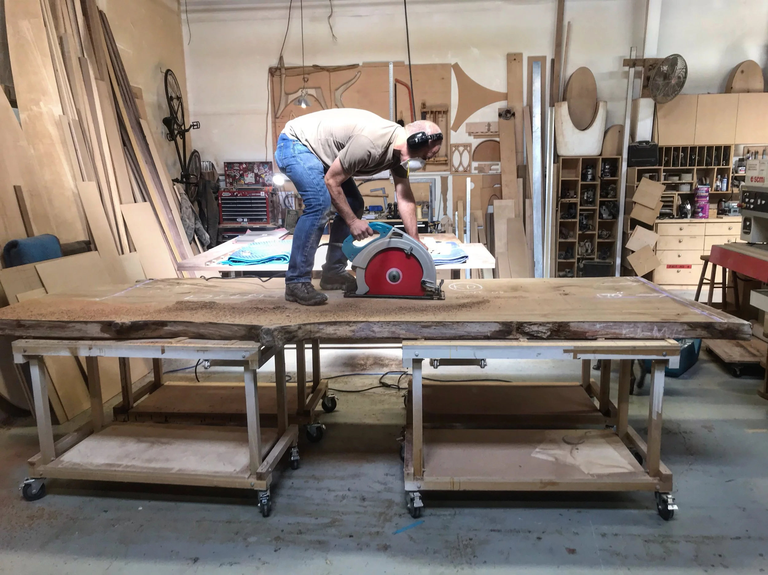 A man cutting a large piece of wood with a circular saw in a woodworking shop.