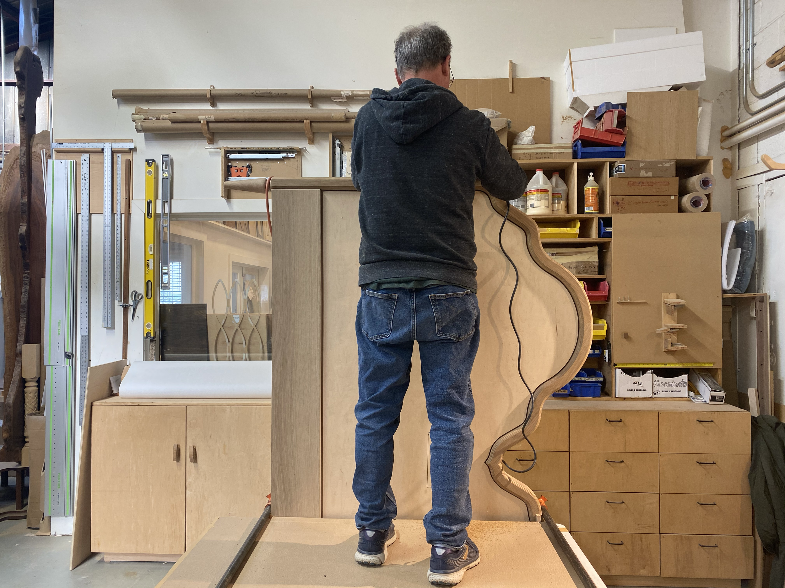 A person working on a woodworking project in a workshop, assembling a wooden piece with a wavy design.