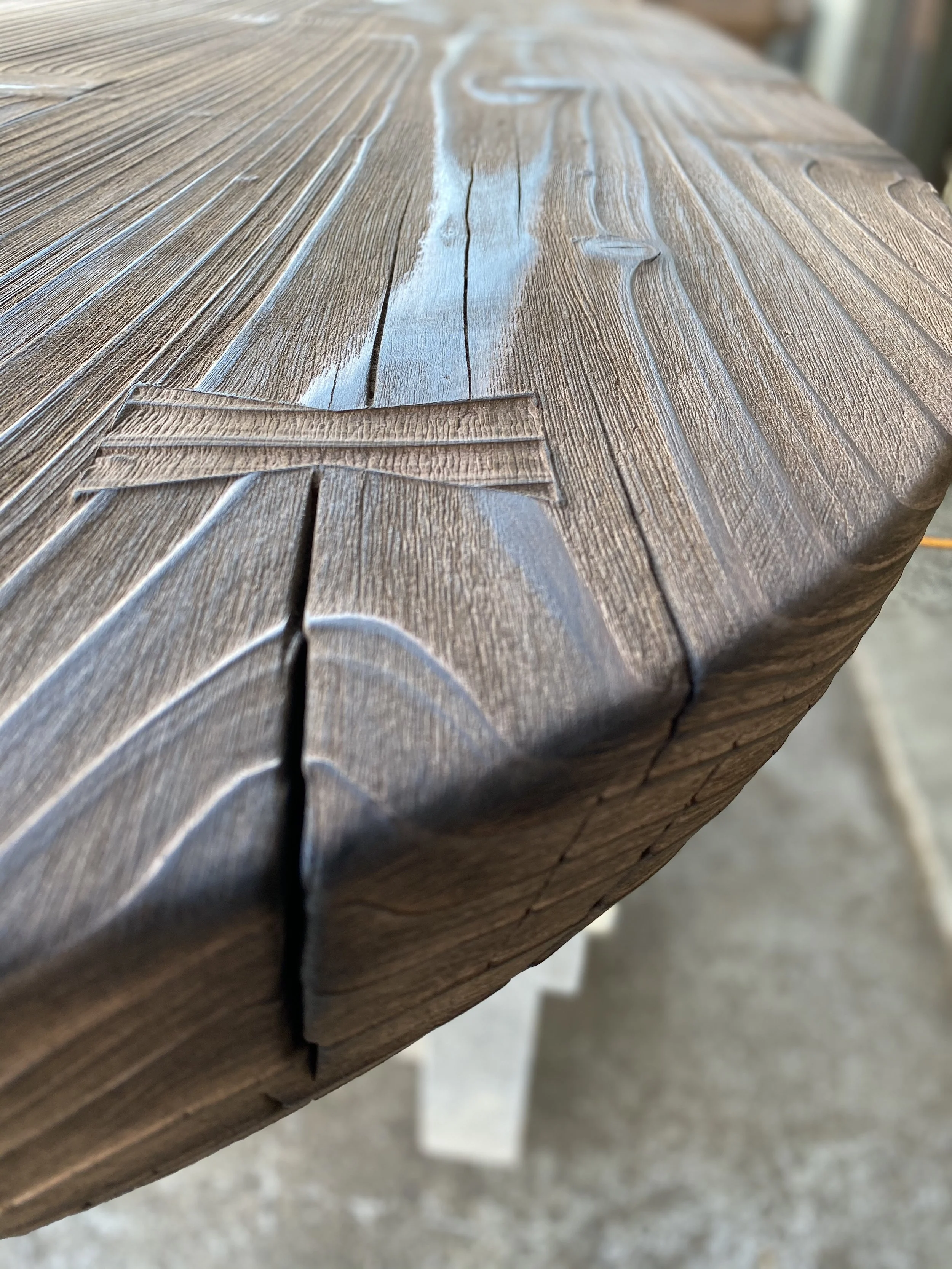 Close-up of a wooden table with a natural finish, showing the wood grain, knots, and cracks in the surface.