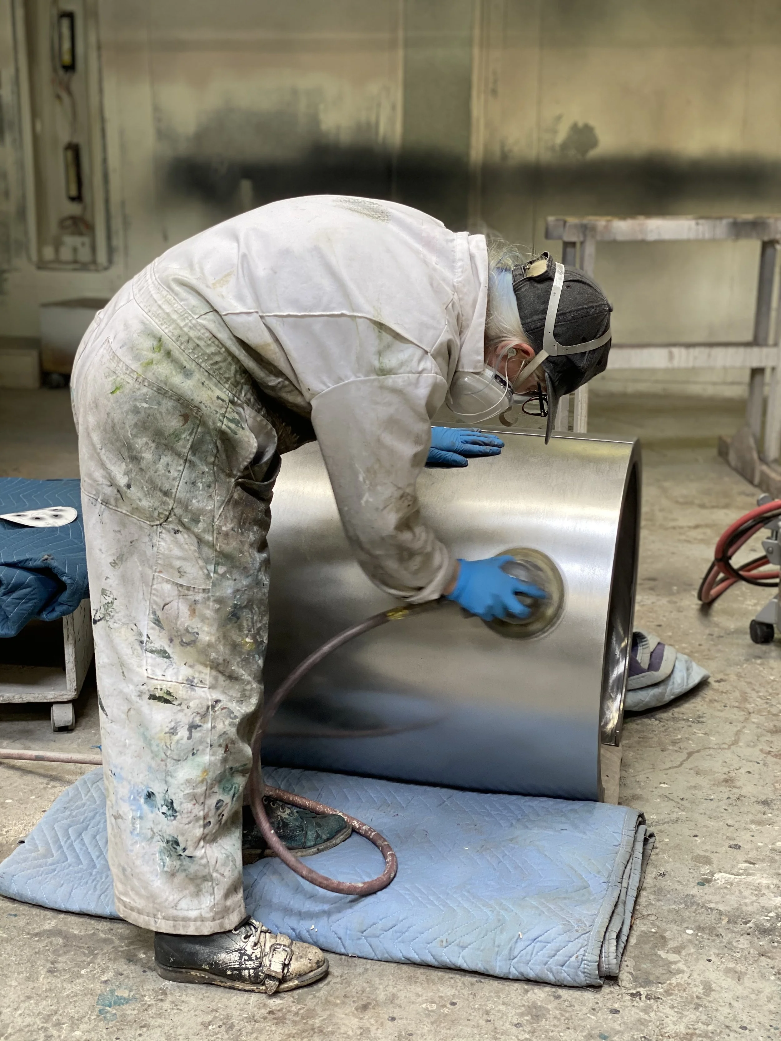 A person wearing protective gear sanding a shiny metal surface in a workshop.