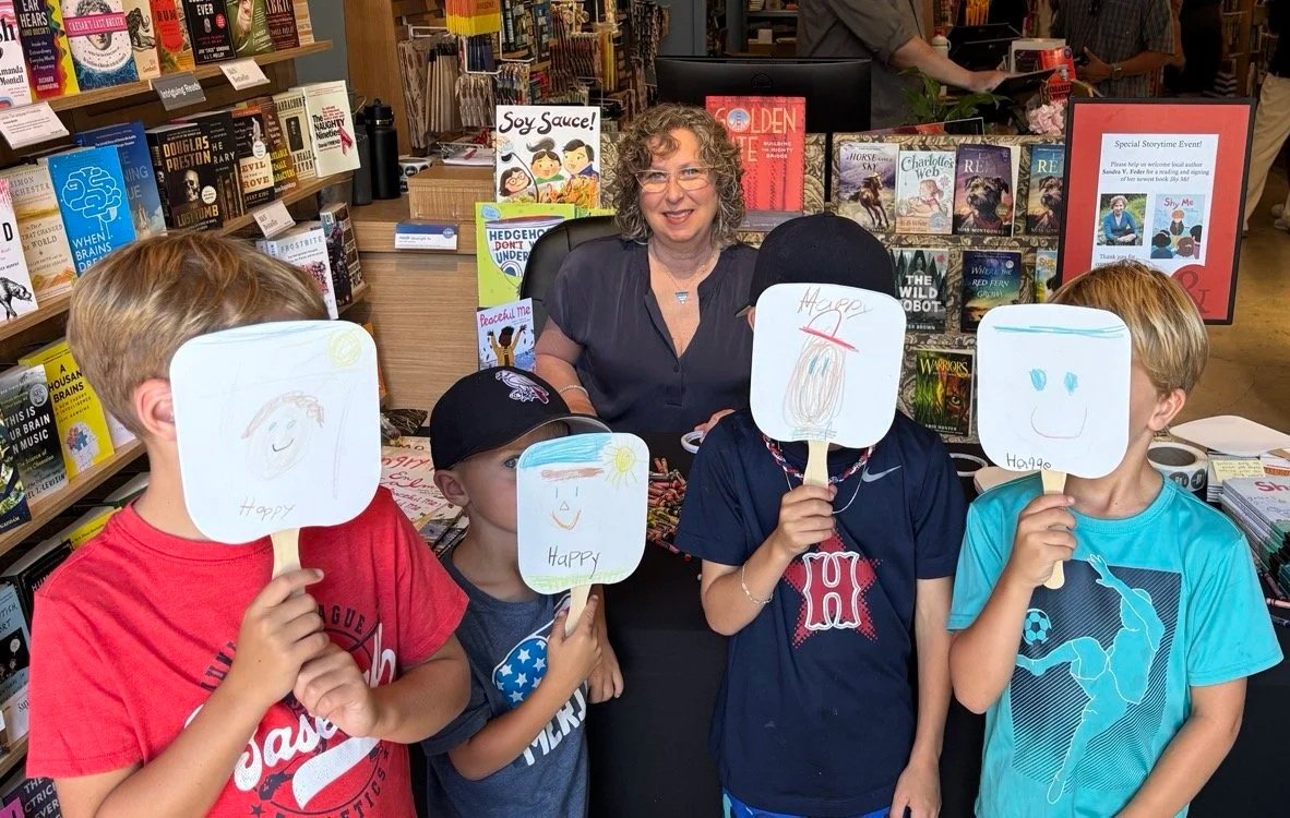 Group of kids at a bookstore event holding up masks with drawings of happy emotions