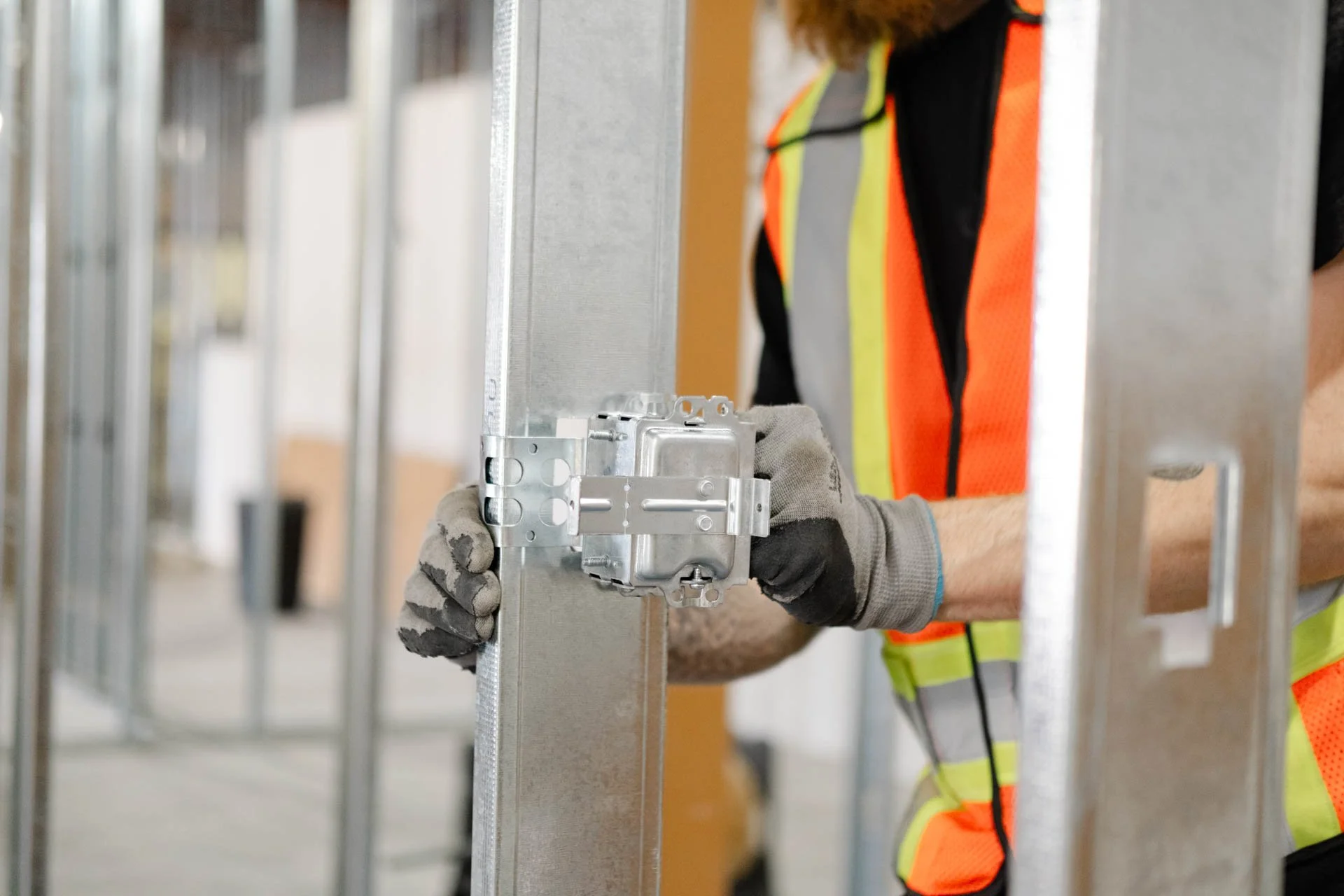 Worker installing an electrical box on a metal wall frame in a construction site