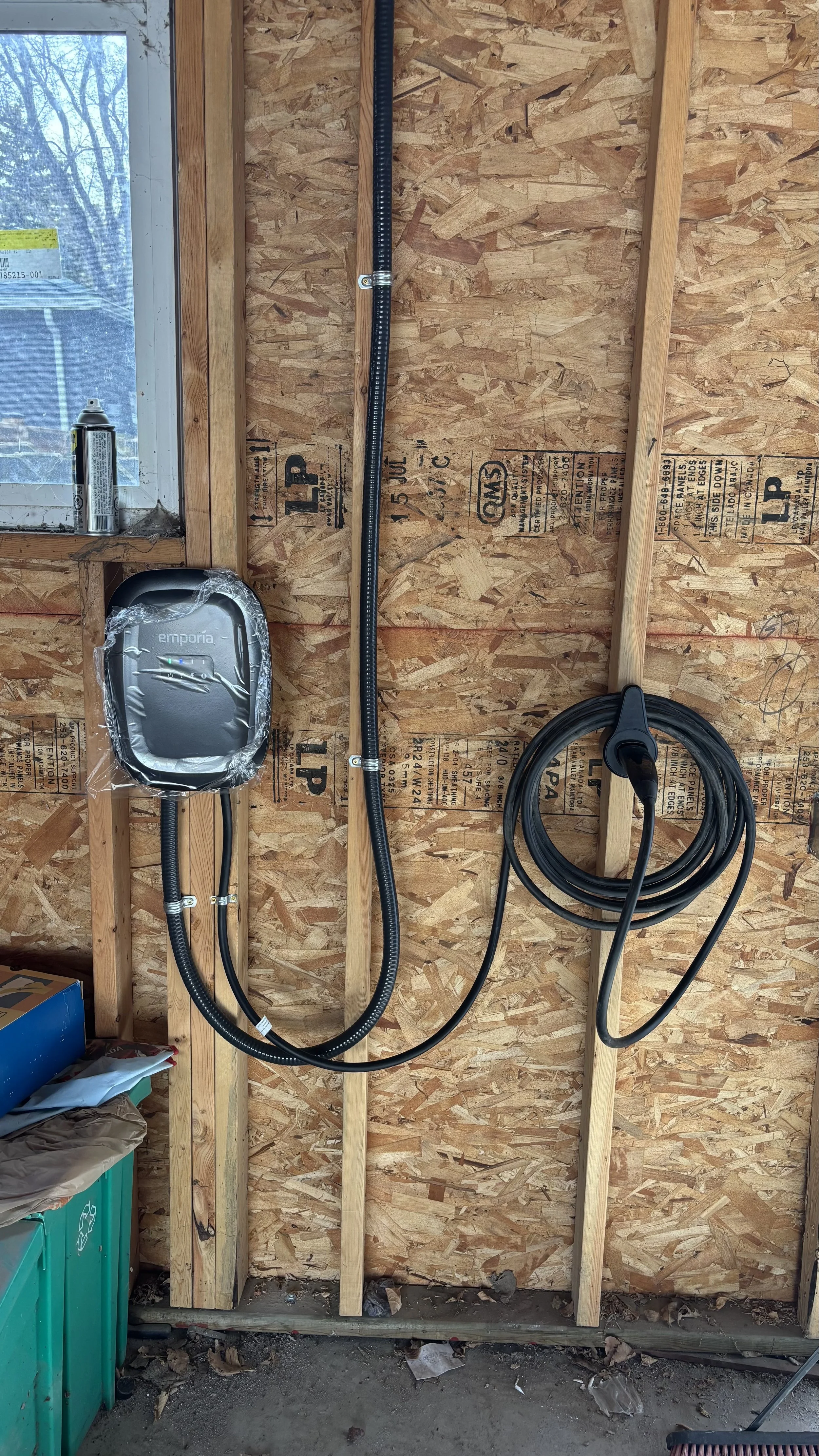 Electrical wiring and outlets installed on unfinished drywall in a construction site with a window and miscellaneous tools and materials.