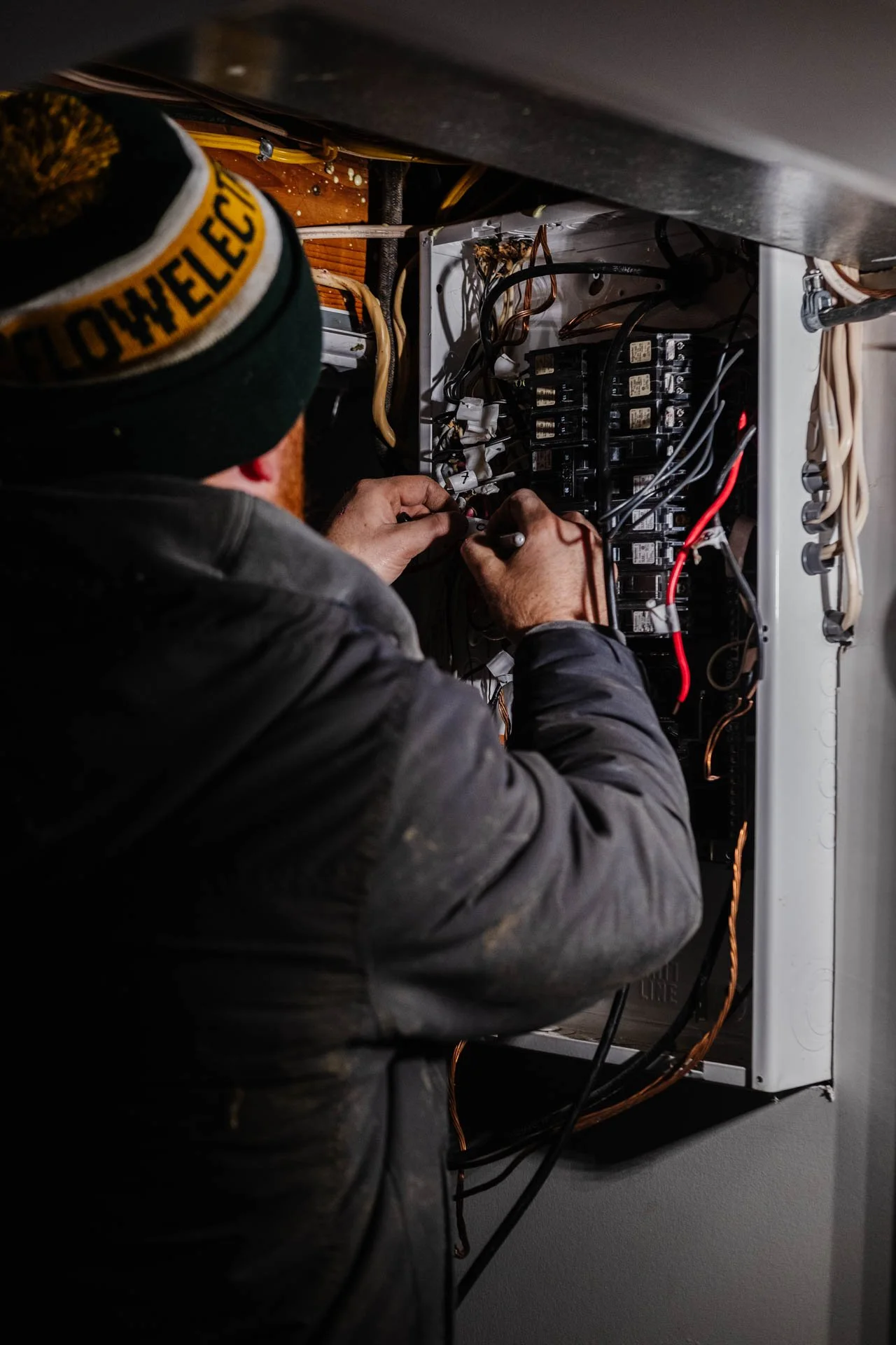 A technician working inside an electrical panel, connecting or inspecting wires, with a focus on the multiple black relays and various colored wires inside the box.