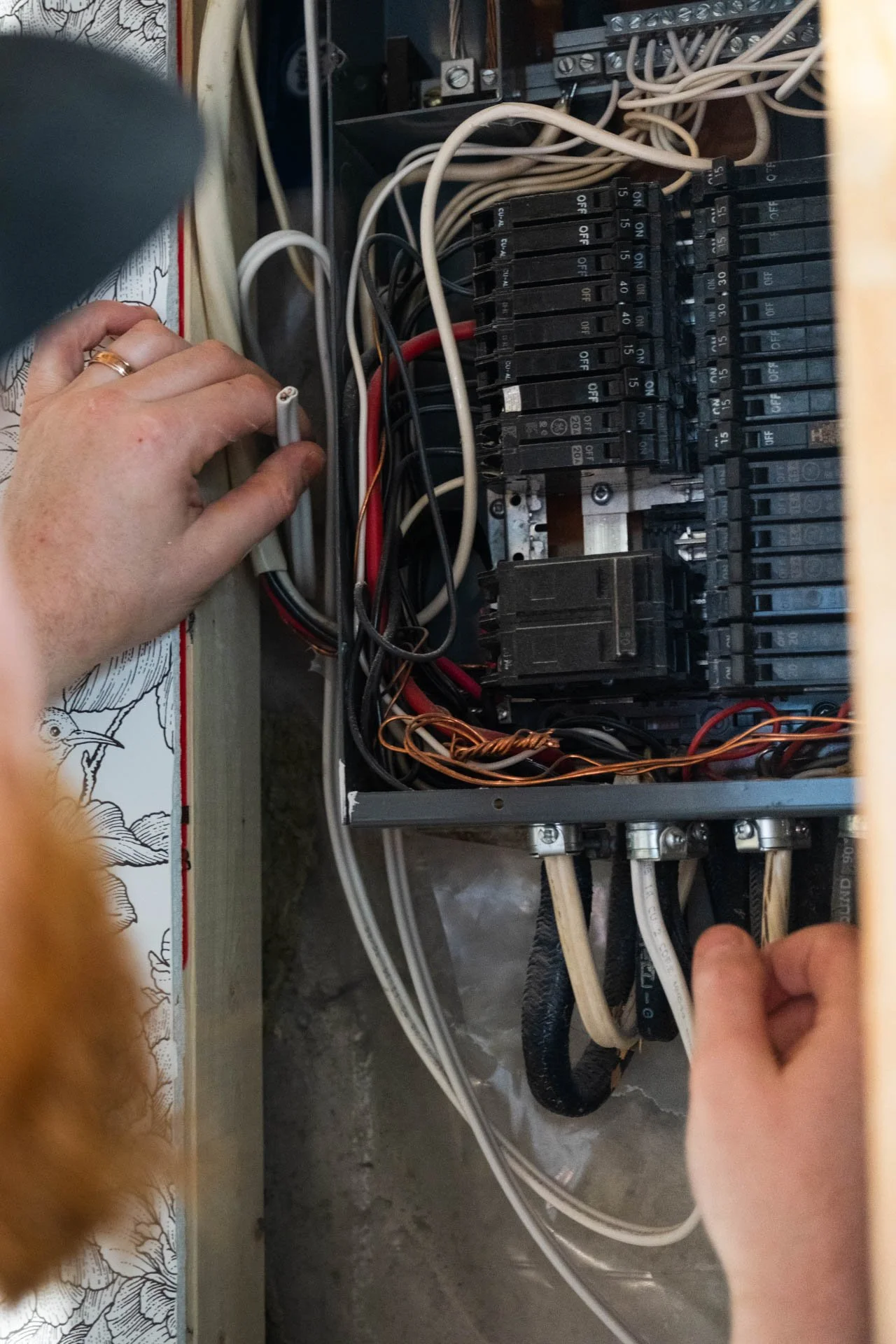 A person's hands working inside an electrical panel with various wires and circuit breakers.
