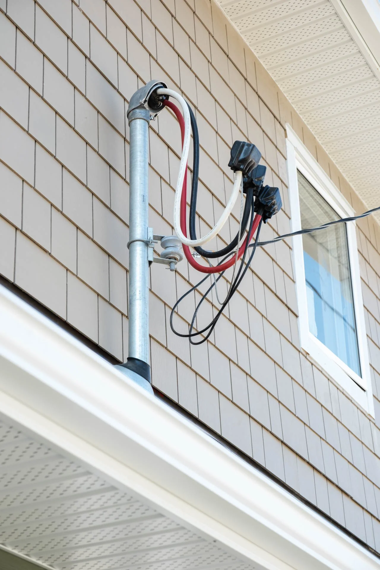 Exterior of a house with an exposed electrical cable setup on the wall near a window.