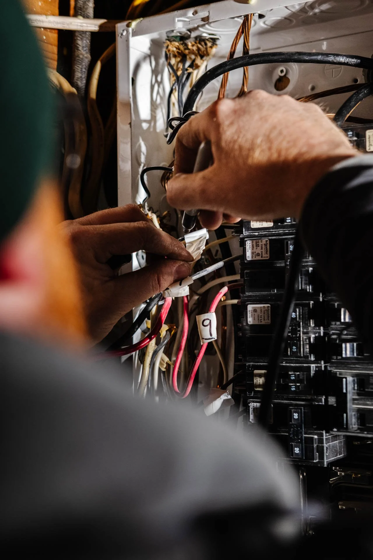 A person working on the wiring inside an electrical panel or fuse box, using a screwdriver to make adjustments or repairs.