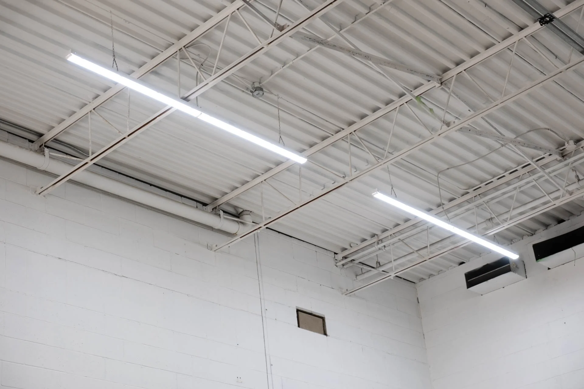 Interior of an industrial or warehouse space with white walls, a metal ceiling, and fluorescent lighting fixtures.