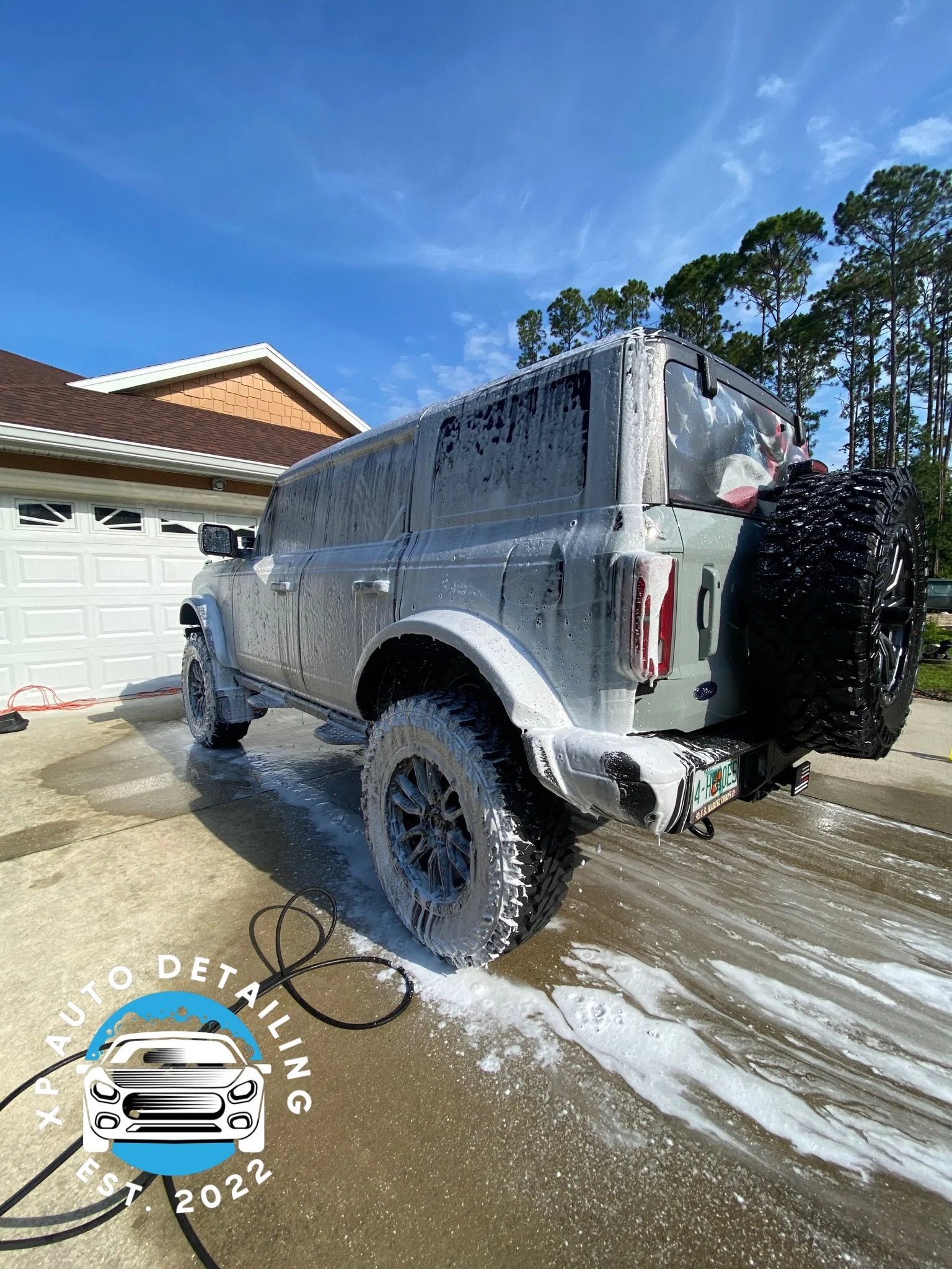 SUV being washed with soap at a driveway, with "XP Auto Detailing Est. 2022" logo in the corner.