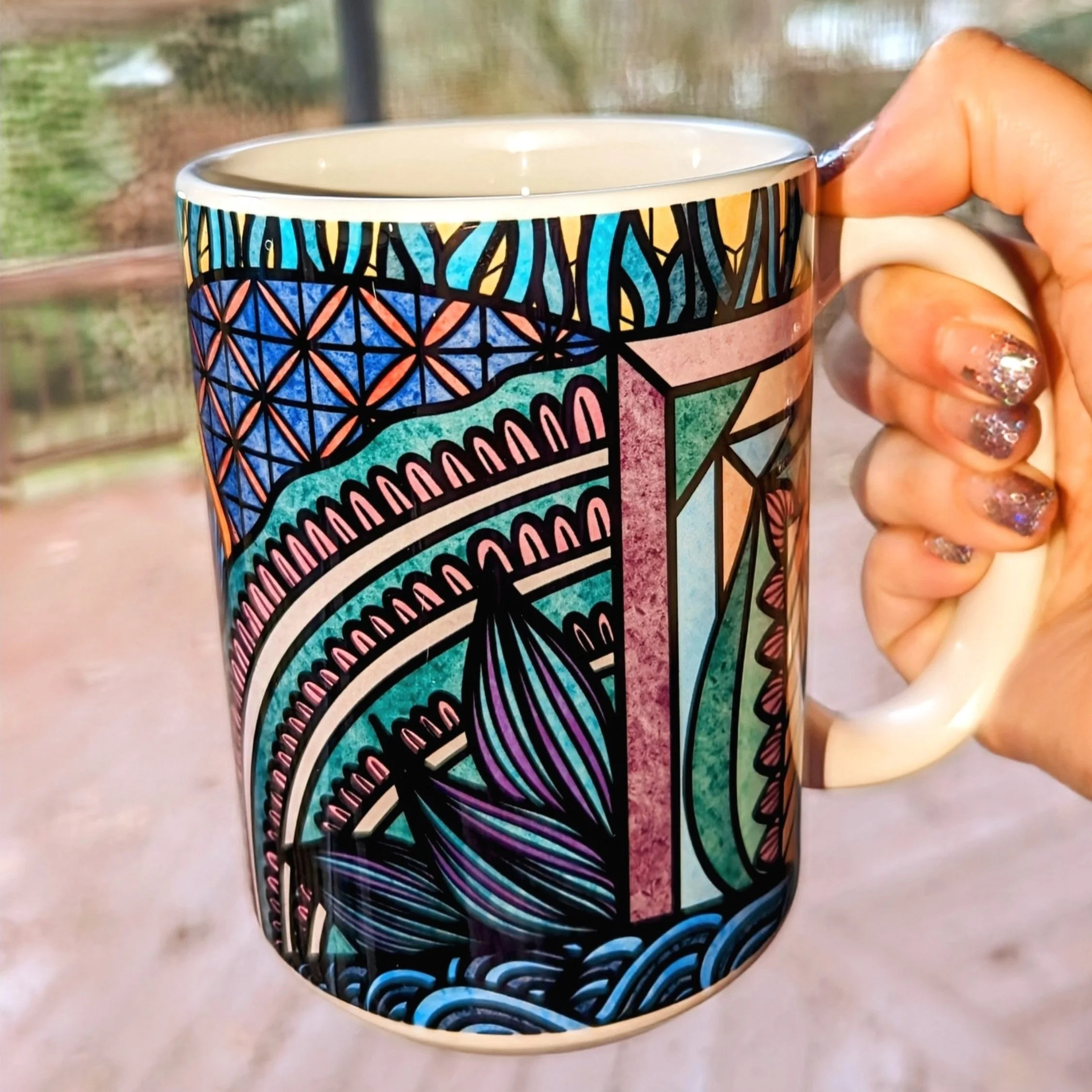Hand holding a colorful ceramic mug with intricate geometric and abstract patterns in blue, green, purple, and orange hues.