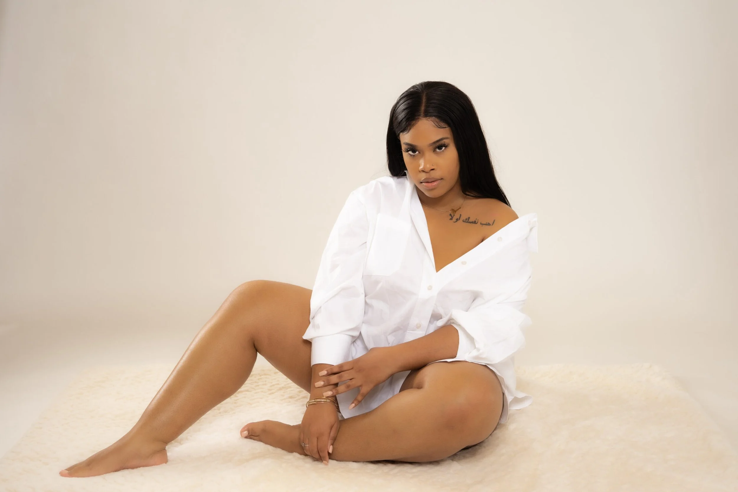 Person with long black hair sitting on a fluffy surface, wearing an oversized white shirt.