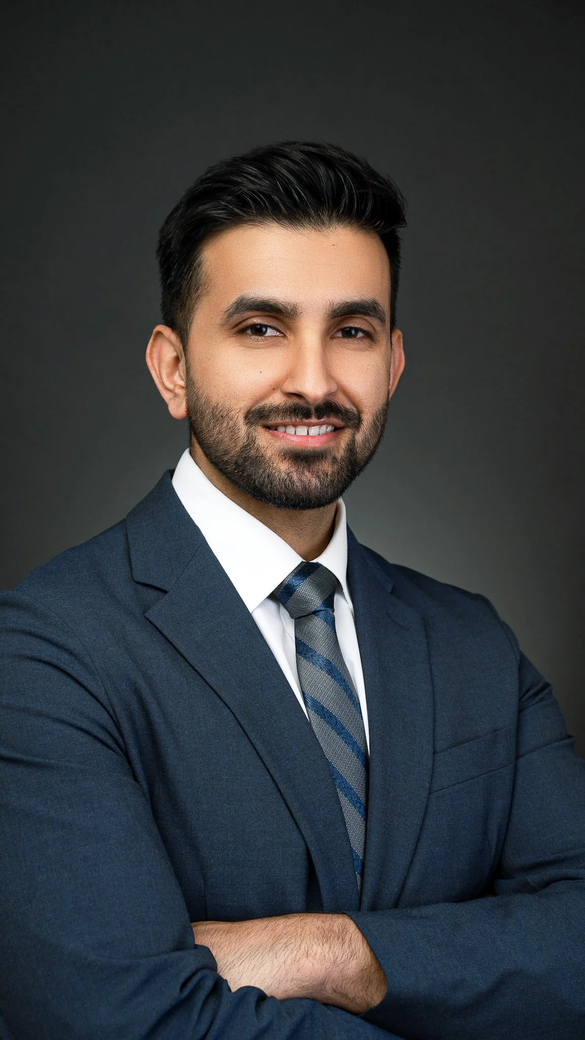 Man in a blue suit smiling against a dark background.