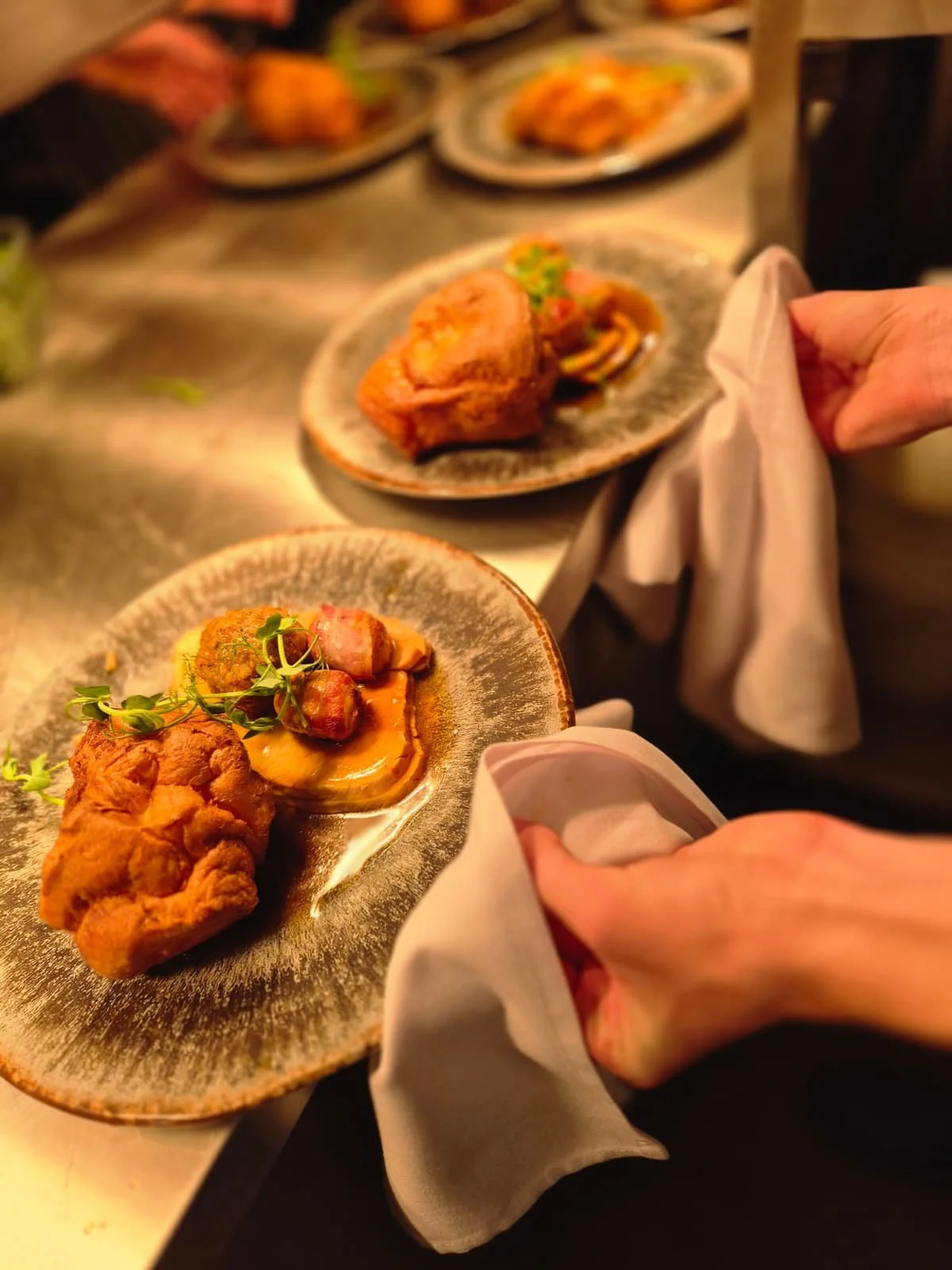 Plates of gourmet food, including fried chicken, vegetables, and garnishes, served on decorative plates in a restaurant setting.