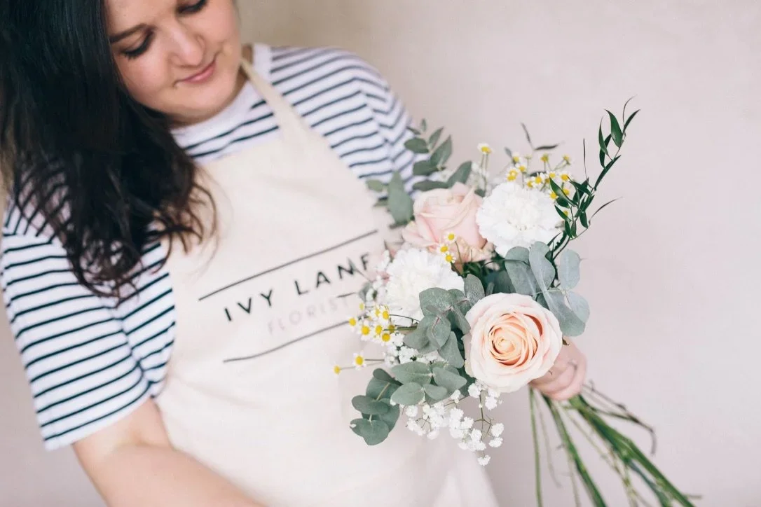 A woman in a striped shirt holding a bouquet of pink and white flowers with greenery.