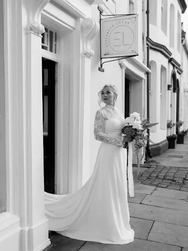 A woman in a wedding dress holding a bouquet of flowers standing on a city sidewalk outside a building.