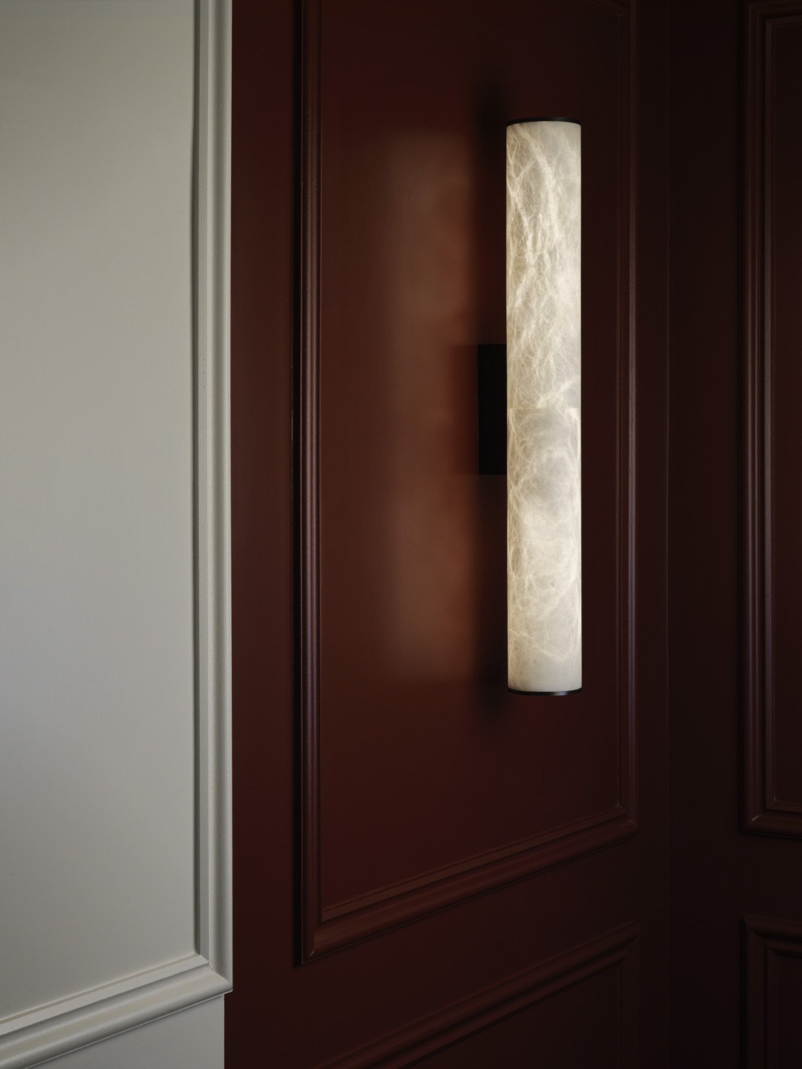 A tall cylindrical wall lamp with a marble-like pattern mounted on a dark wooden wall panel.