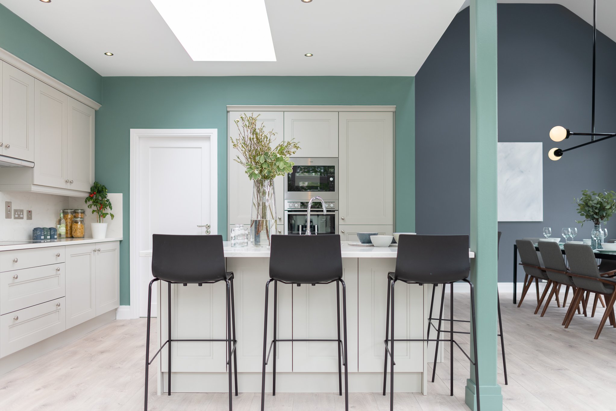 Modern kitchen with white cabinetry, a large island with four black chairs, a blue accent wall, and a dining area with a table set for six.