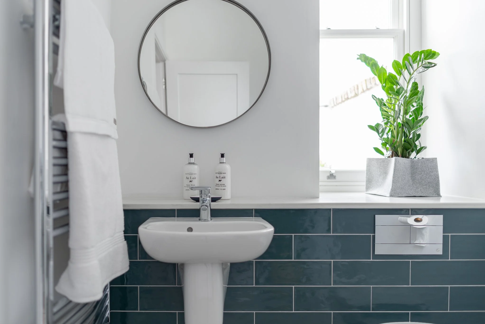 white bathroom with teal subway tiles and round mirror