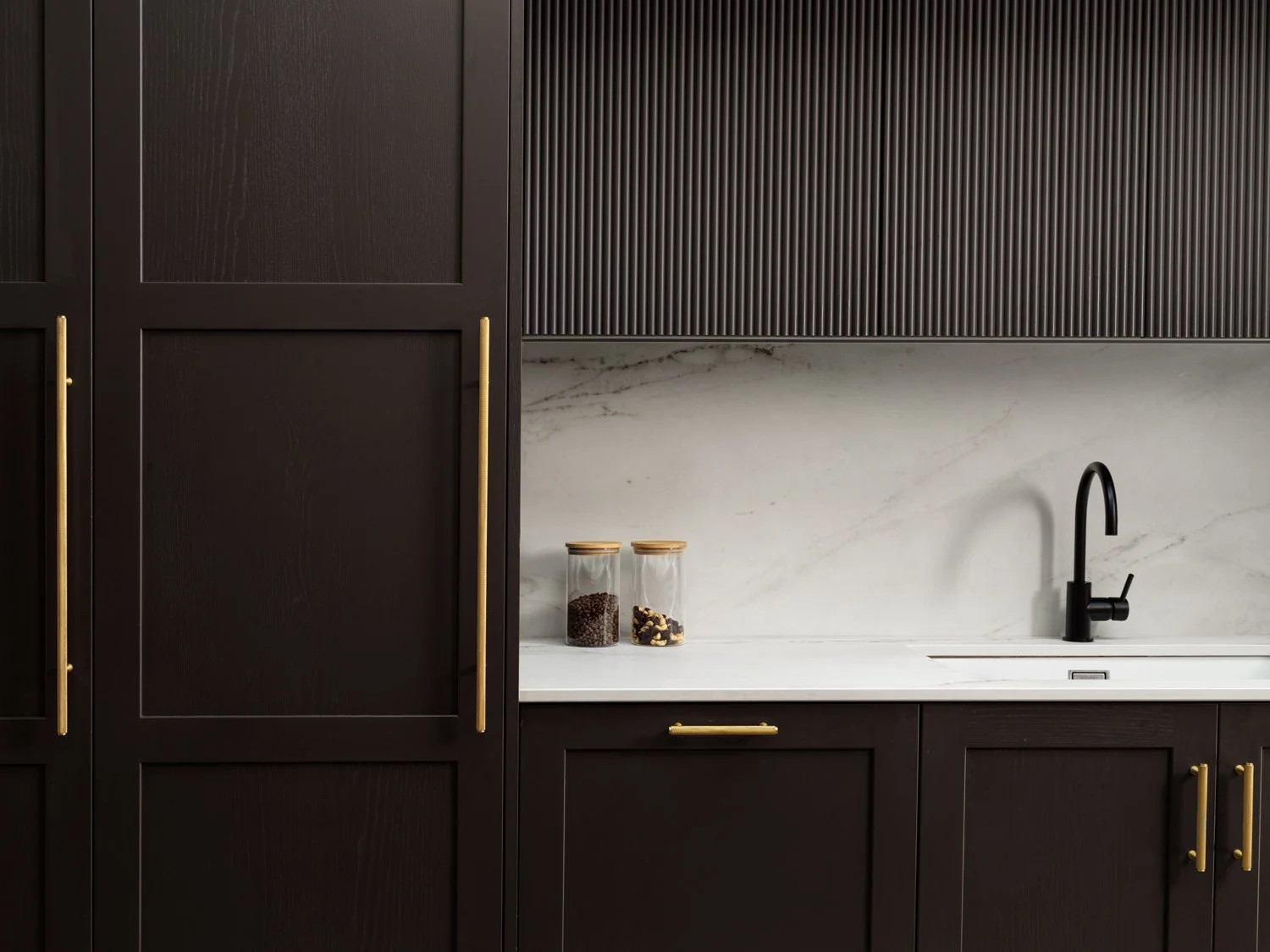 brown kitchen cabinetry with gold handles and marble backsplash