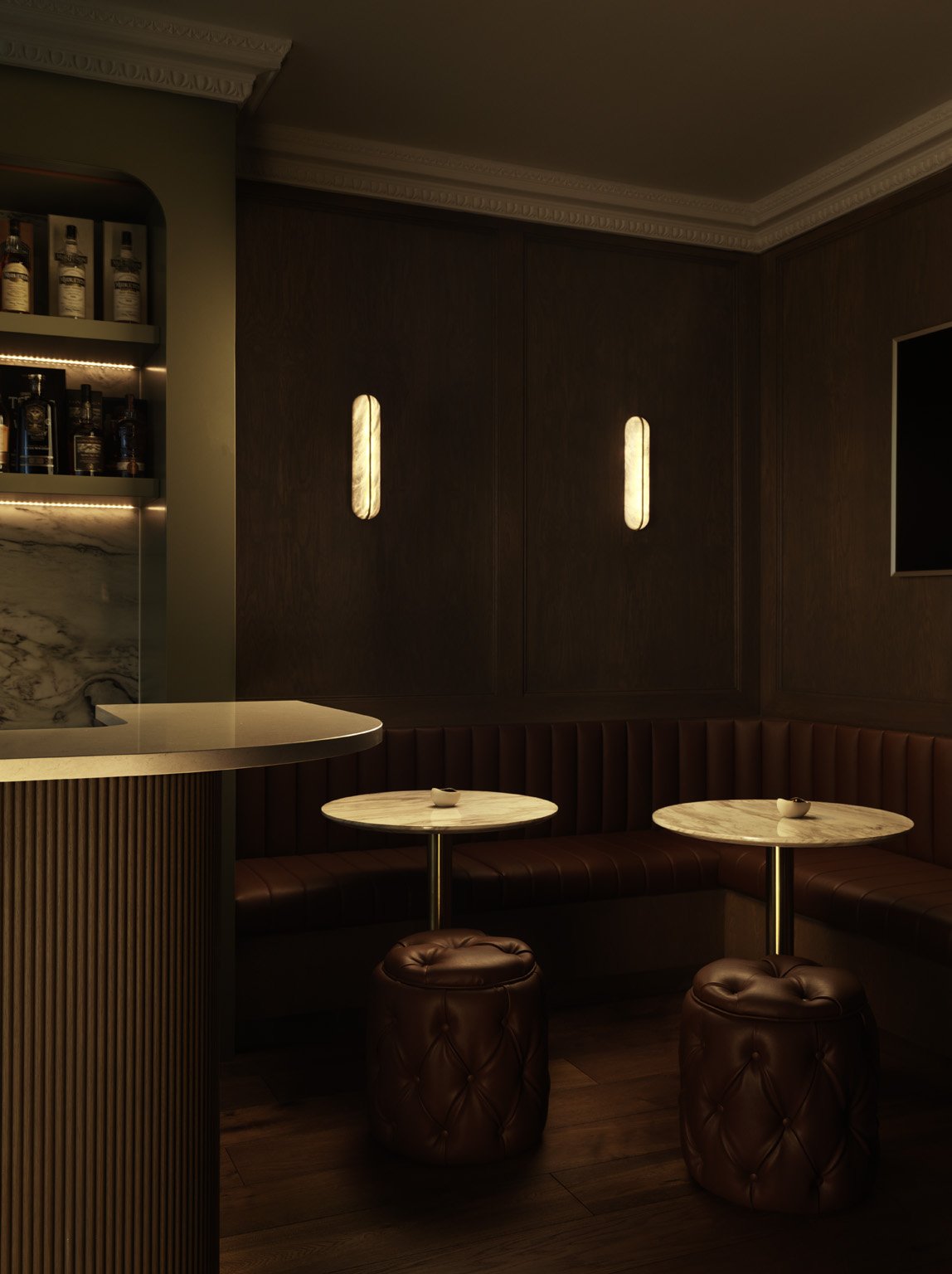 A dimly lit bar with dark wood walls, two small round marble tables, leather stools, and bottles on shelves
