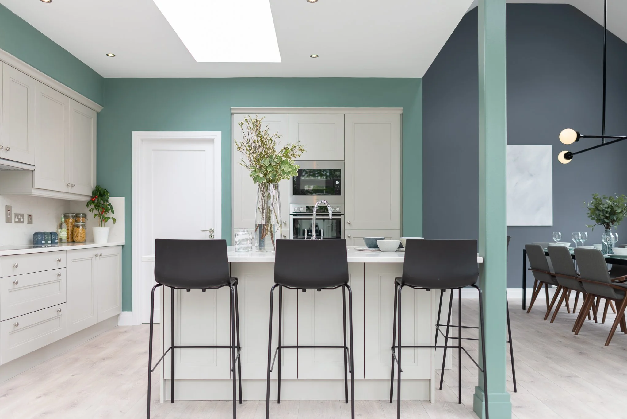 open plan kitchen dining area with  light teal walls and white cabinetry