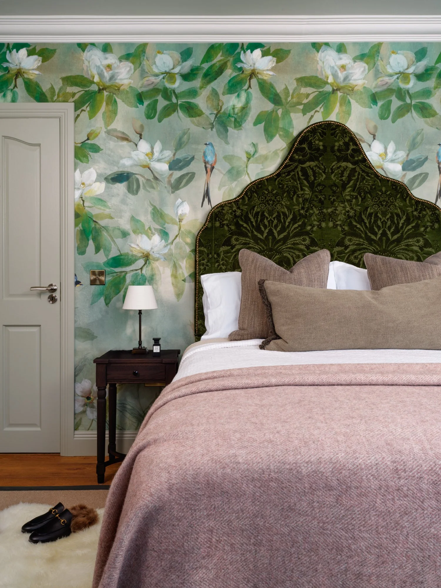 green flowery wallpaper with large dark green vintage headboard and pink throw
