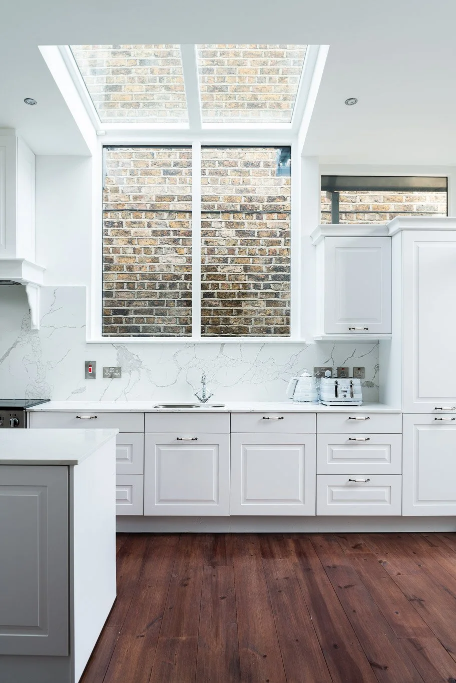 white kitchen with mahogany floors and ceiling glazing.