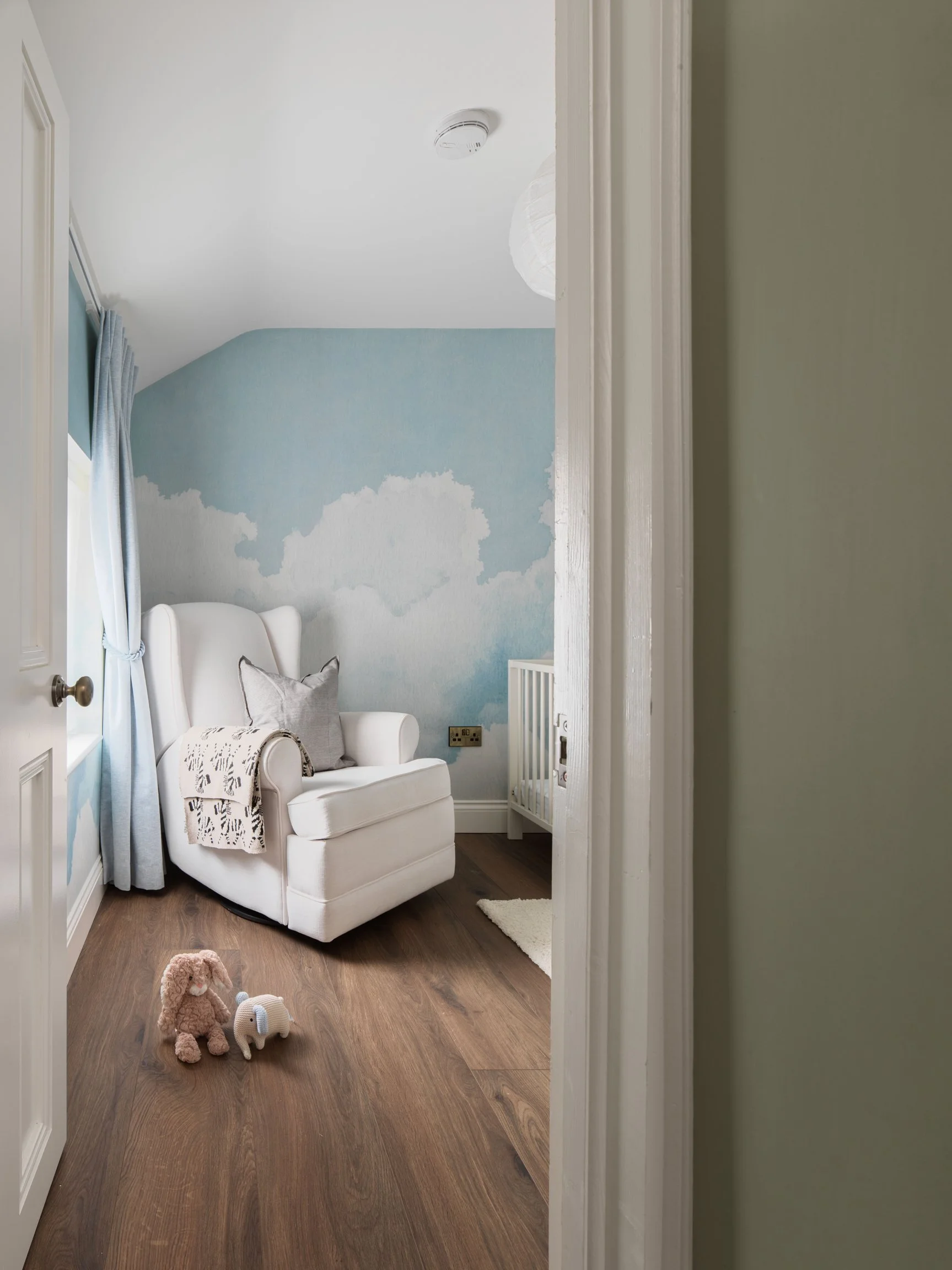 Childs bedroom with sky-blue and clouds painted walls with toys on floor