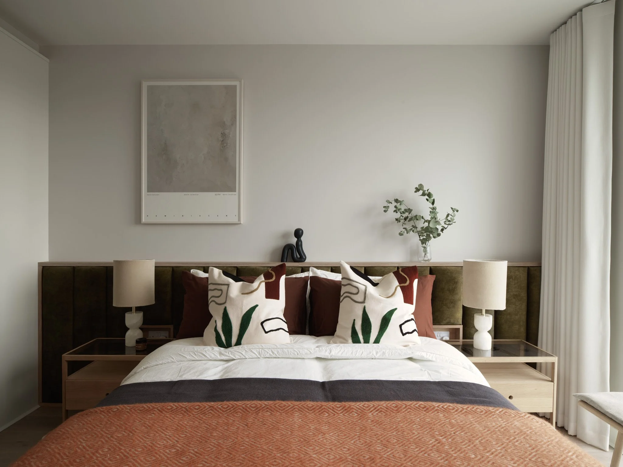cream interior designed bedroom with artwork on wall and rust coloured bed throw
