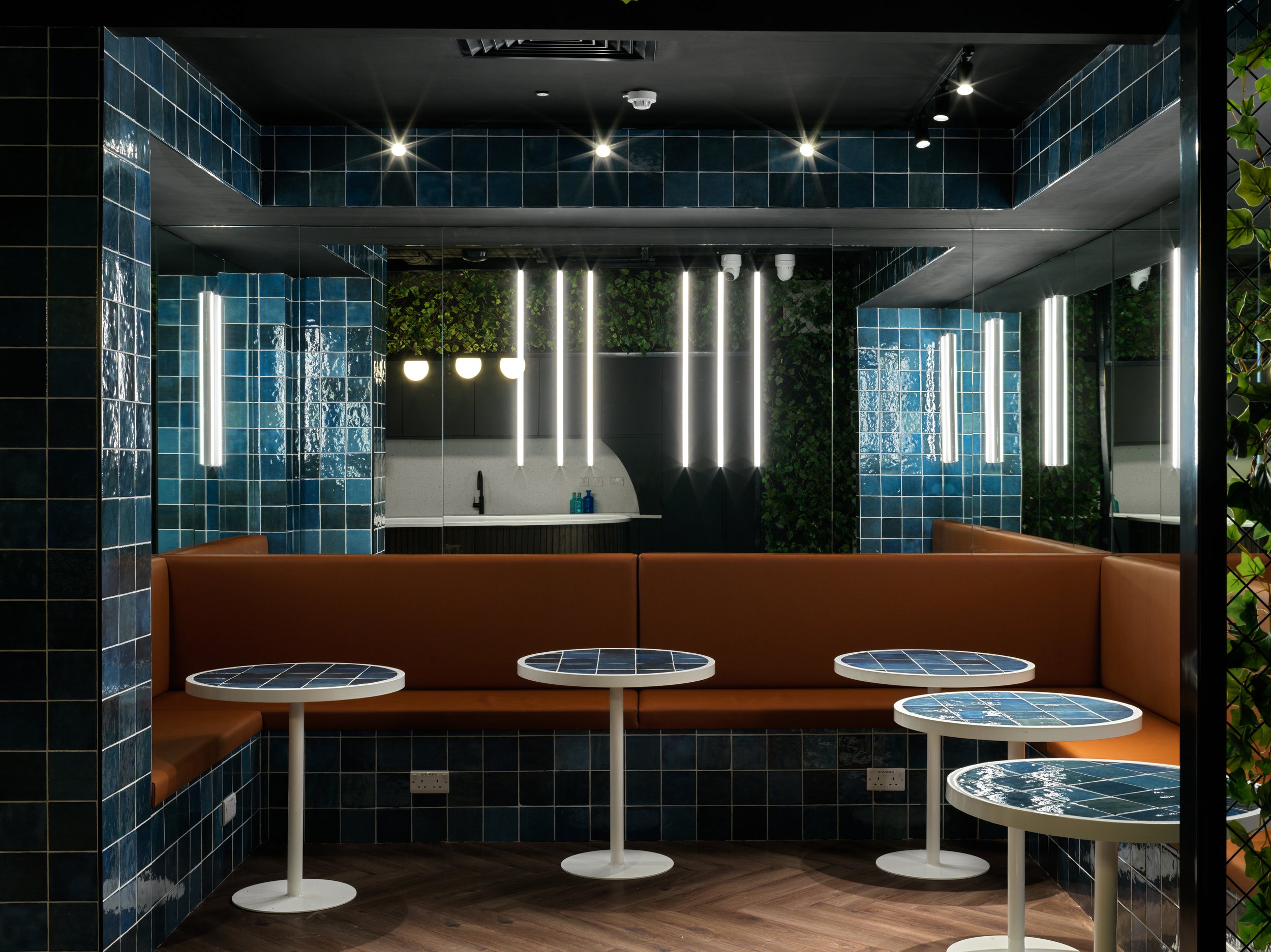 Interior of a modern cafe or lounge with brown cushioned seating and matching round tables with blue ceramic tile tops, reflecting minimalistic and contemporary design.