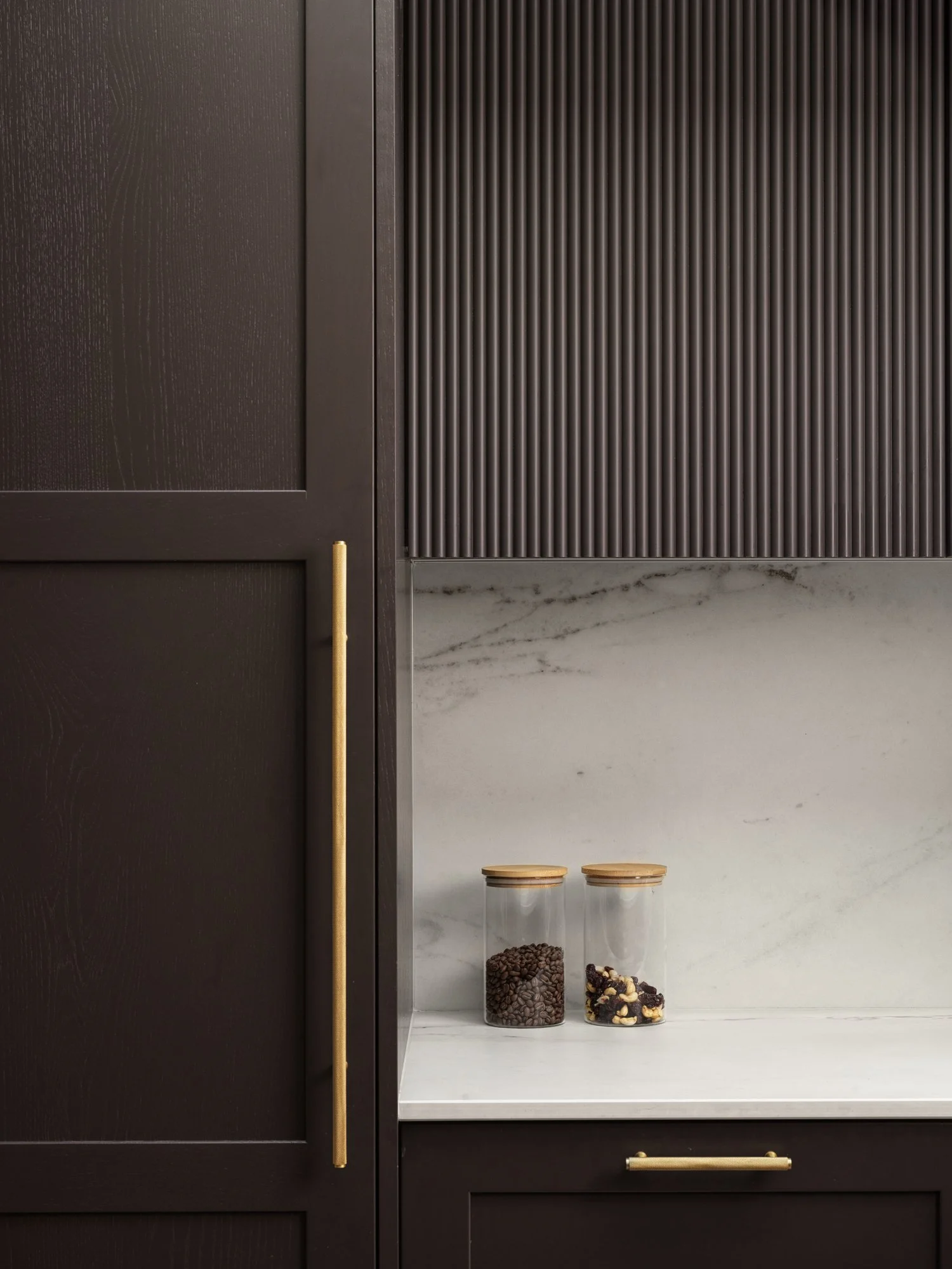 brown kitchen cabinetry with gold handles and marble backsplash