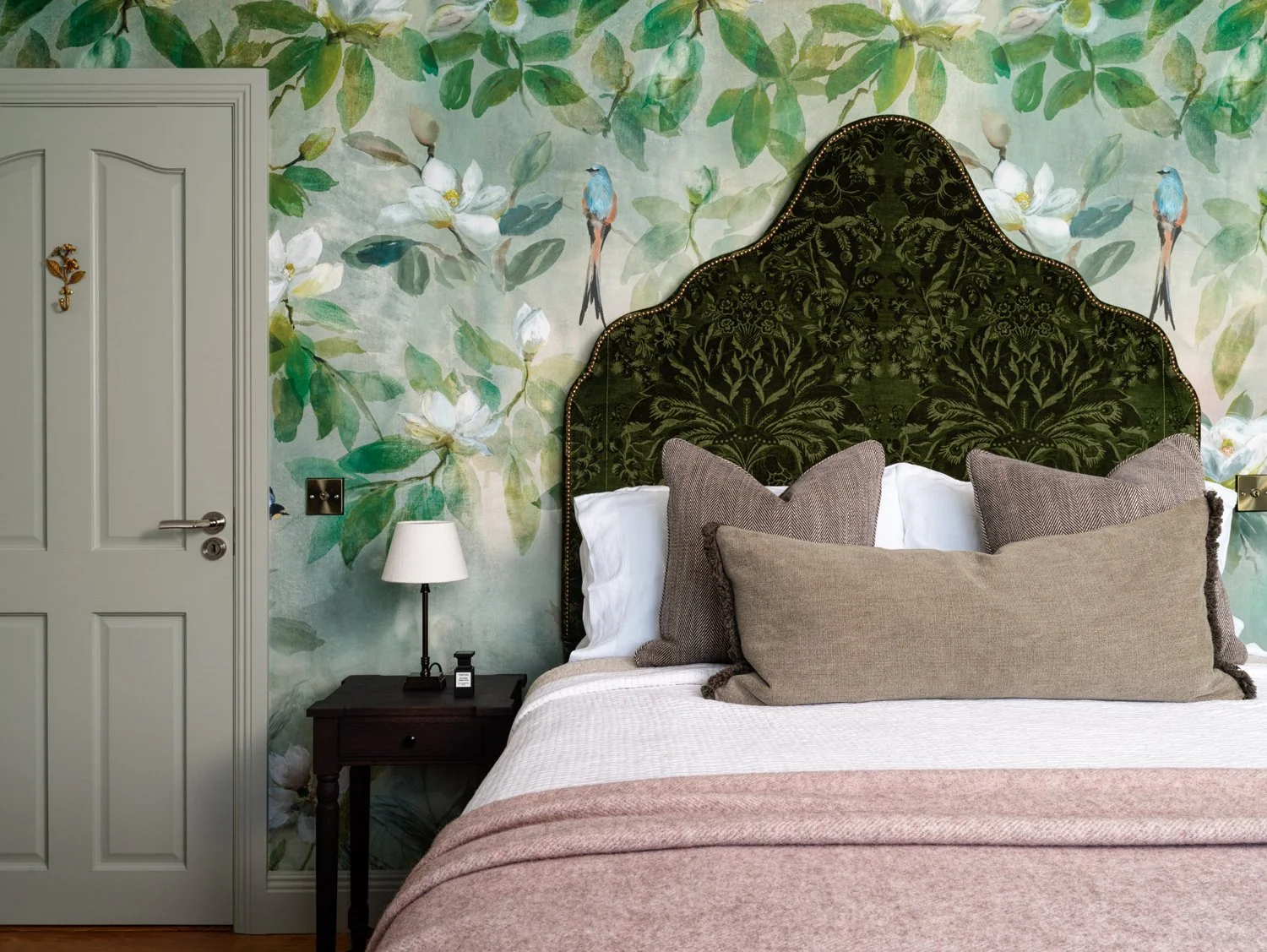 green flowery wallpaper with large dark green vintage headboard and pink throw