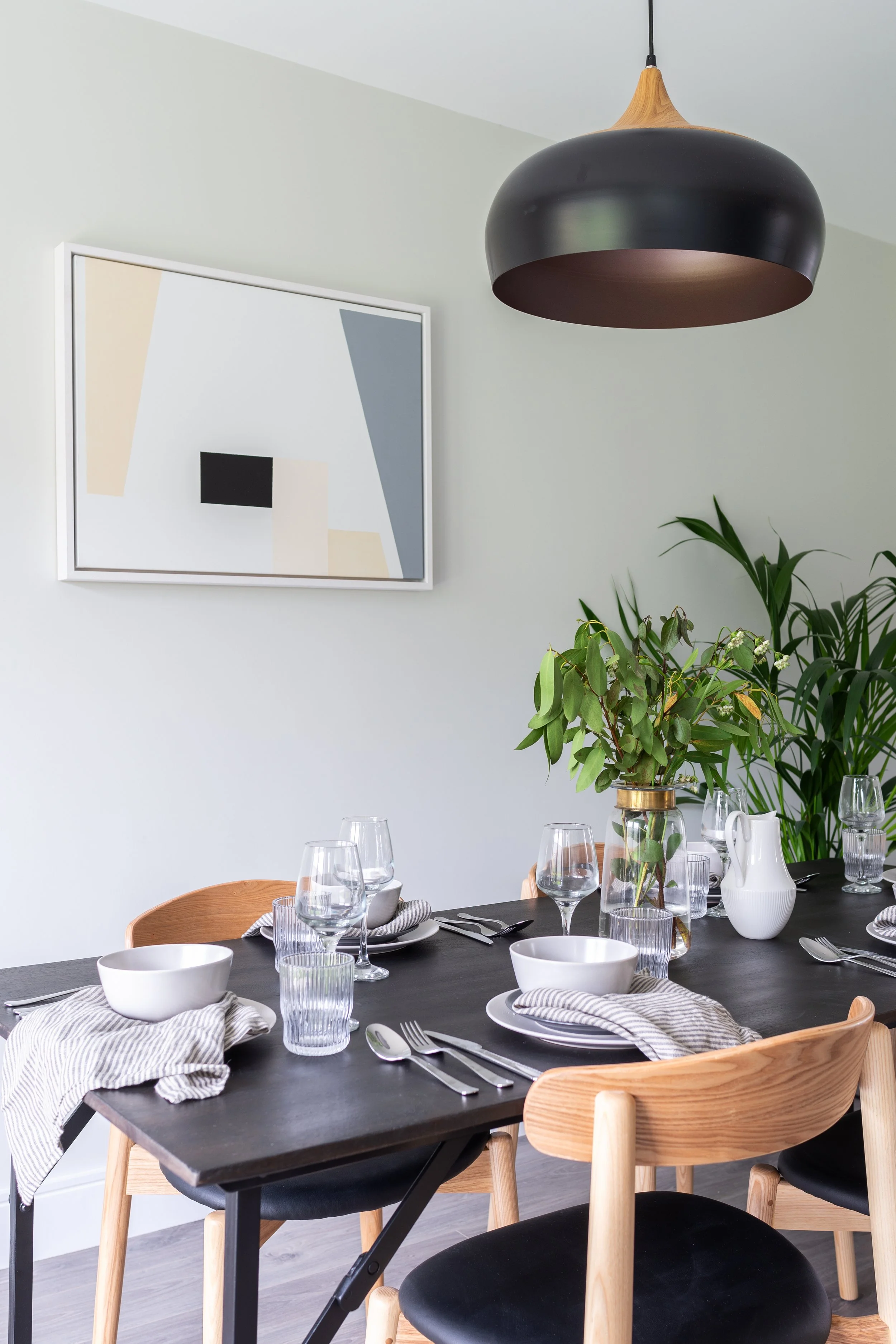 airy dining table with oak and black dining chairs and wall art