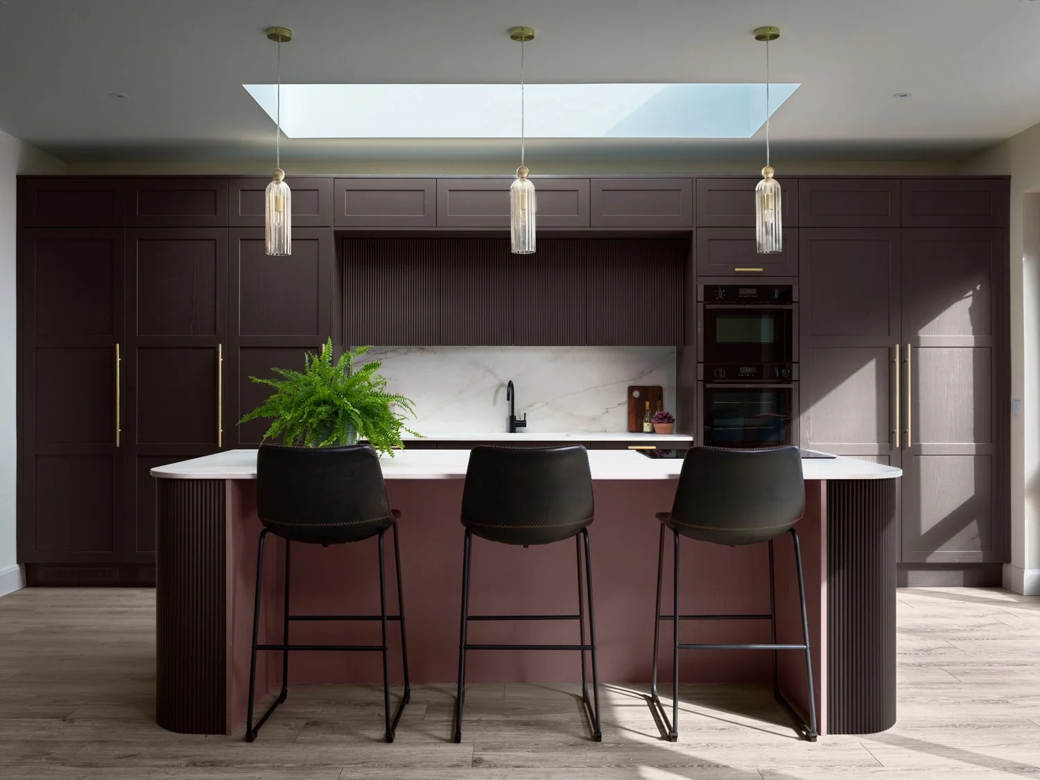 Open plan brown kitchen with curved island and blush pink paint