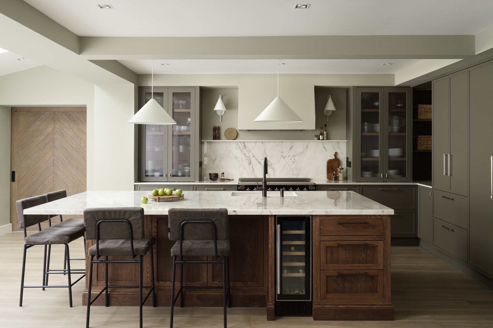 Modern kitchen with a large white marble island with four chairs, gray cabinets, a marble backsplash, and a wine fridge.