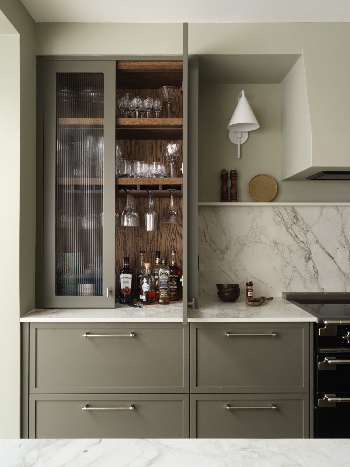 Kitchen cabinet with glassware and liquor bottles, marble countertop, and wall-mounted light fixture