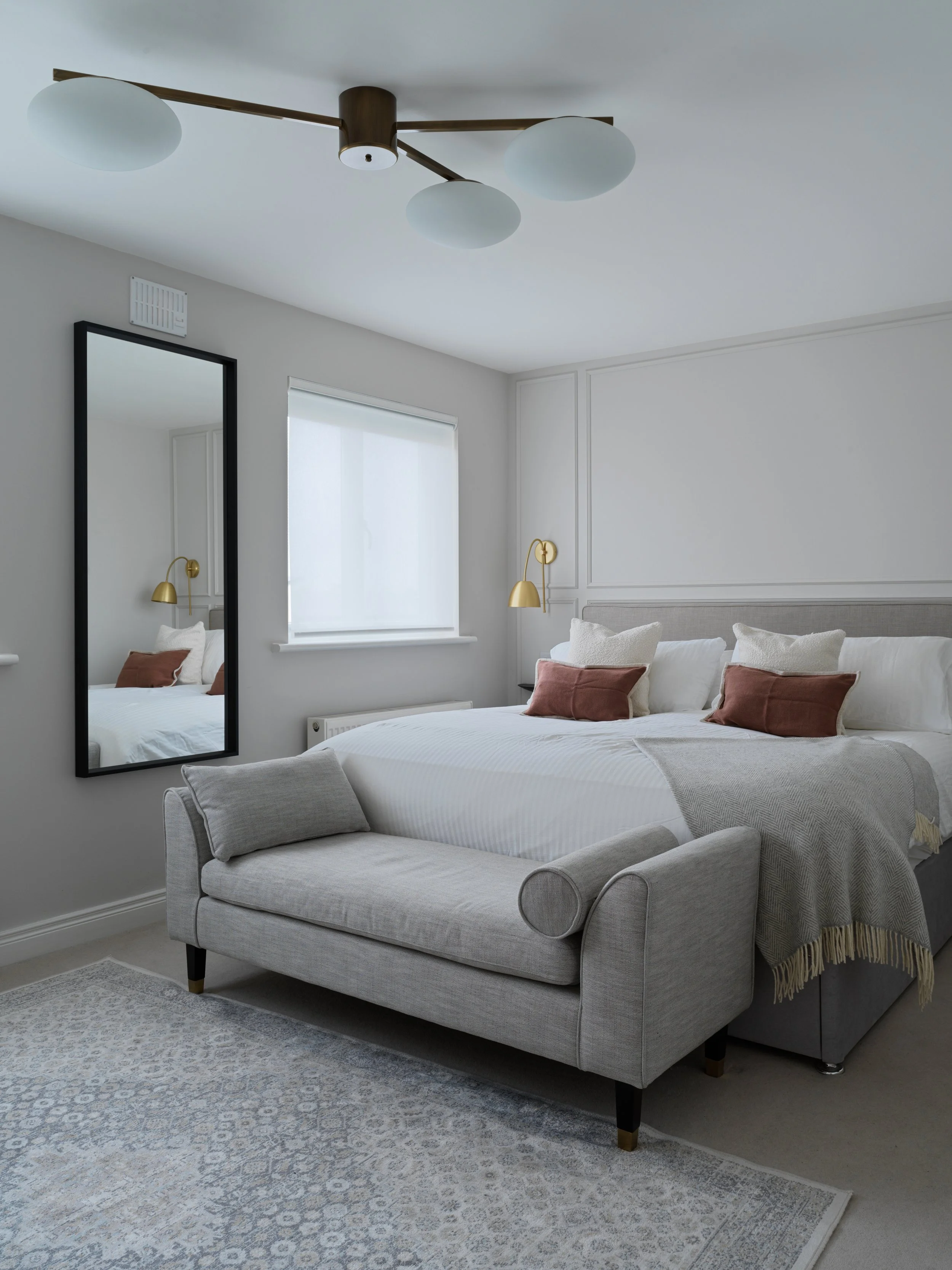 large greige coloured master bedroom with chaise long at foot of bed