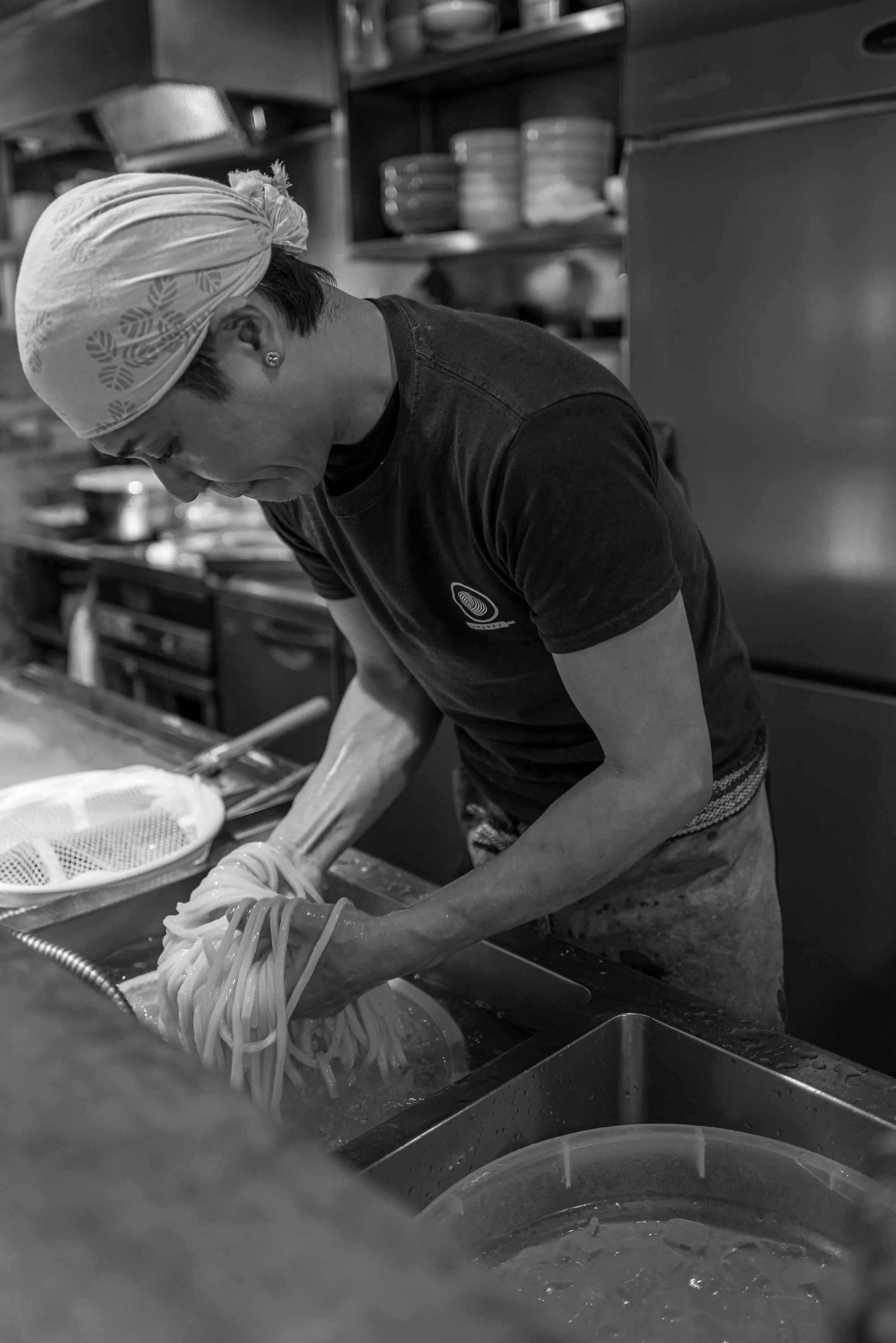 Print AD-0043. A cook handling noodles beside a sink.