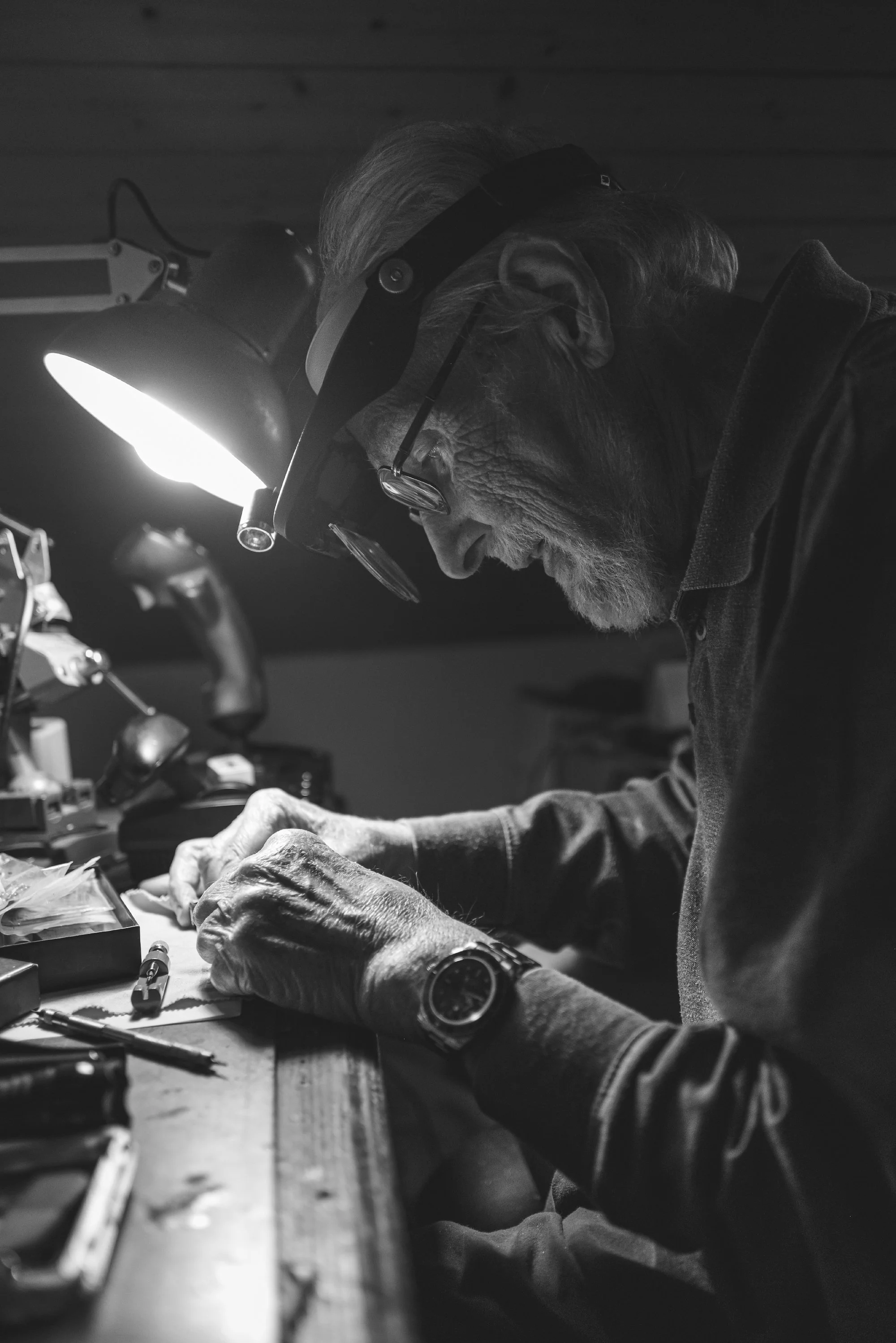 Print AD-0039. A craftsperson concentrating at a lamp-lit workbench.