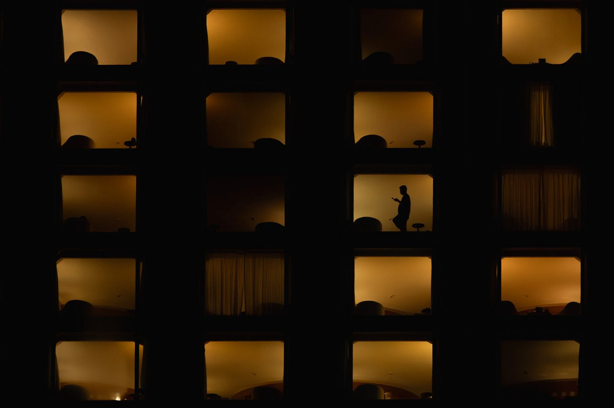 Print AD-0012. Illuminated yellow compartments and silhouettes against a dark facade.