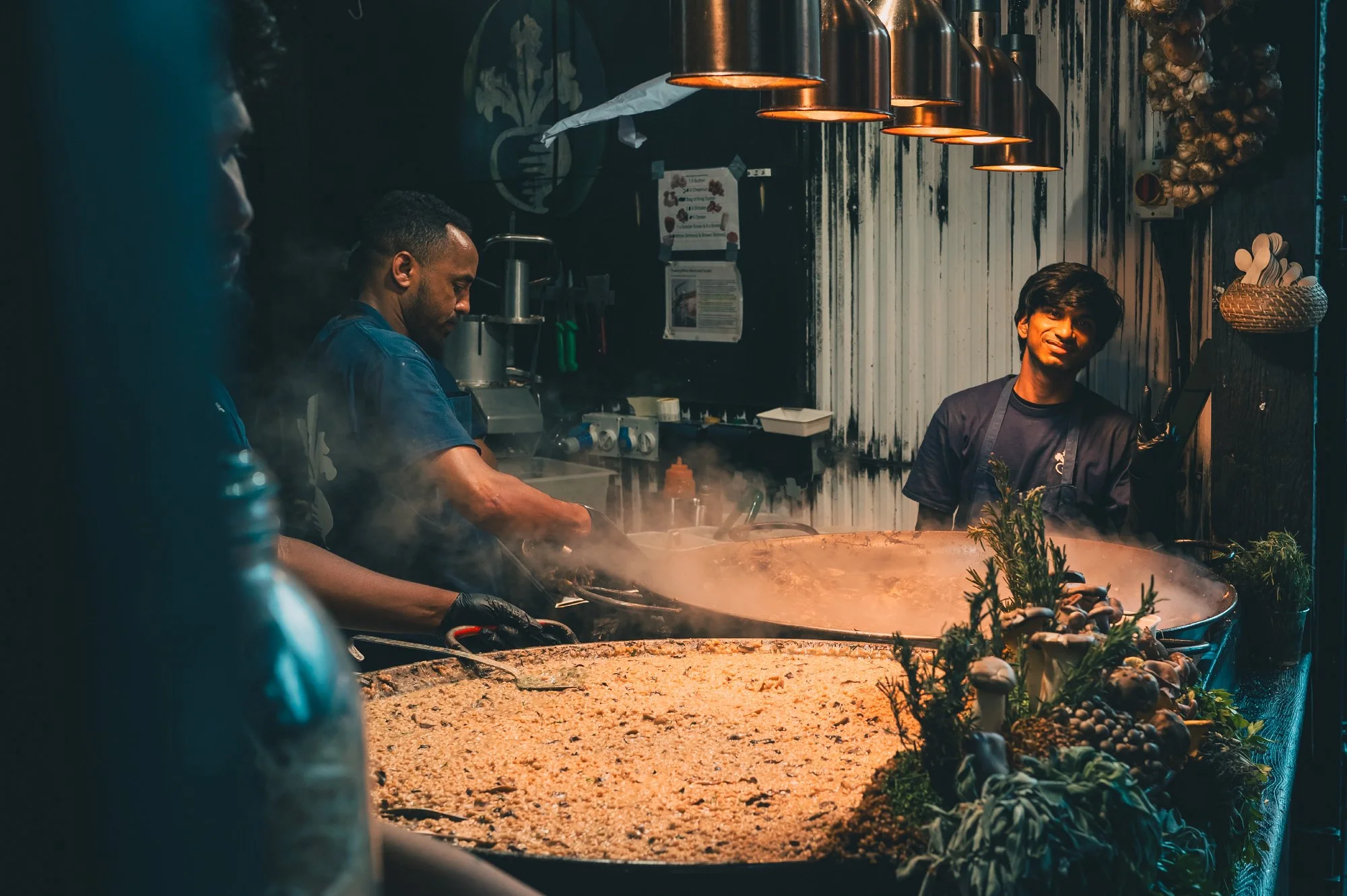 Print AD-0046. Cooks working around large pans beneath warm lamps.