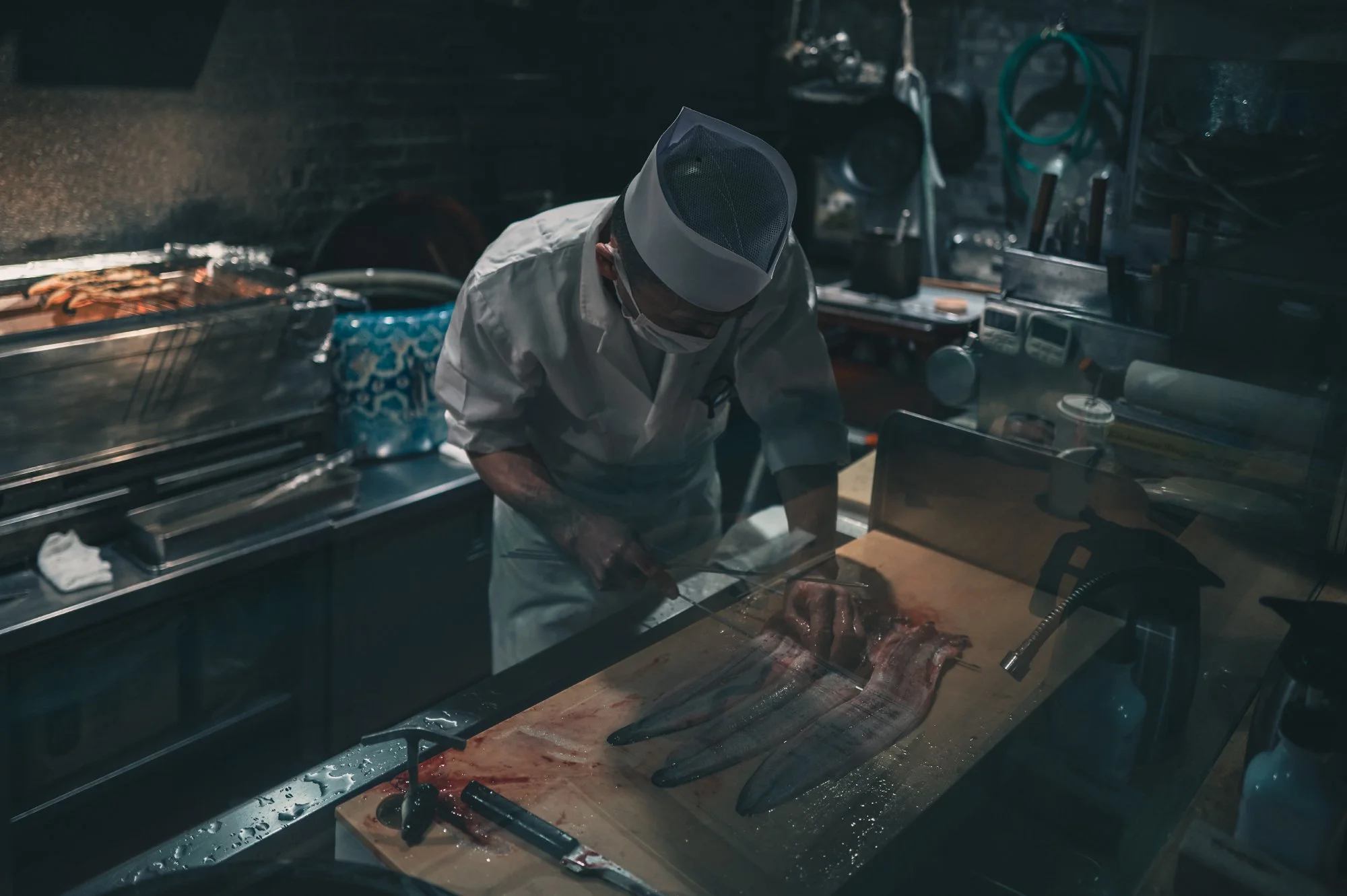 Print AD-0042. A cook preparing fish behind a glass counter.