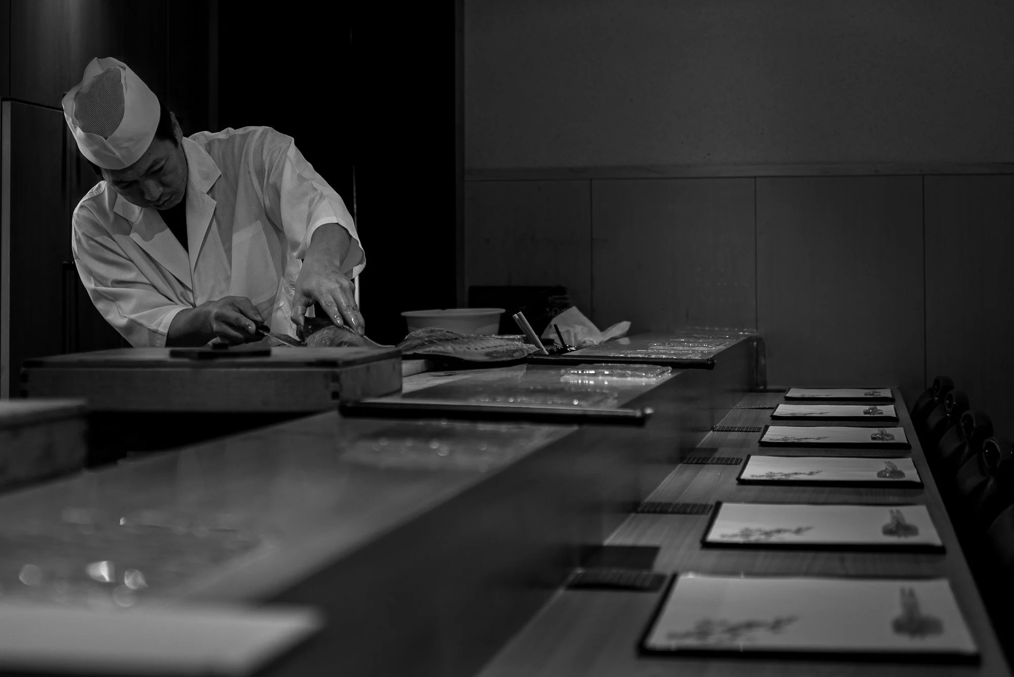 Print AD-0037. A cook working behind a long prepared counter.