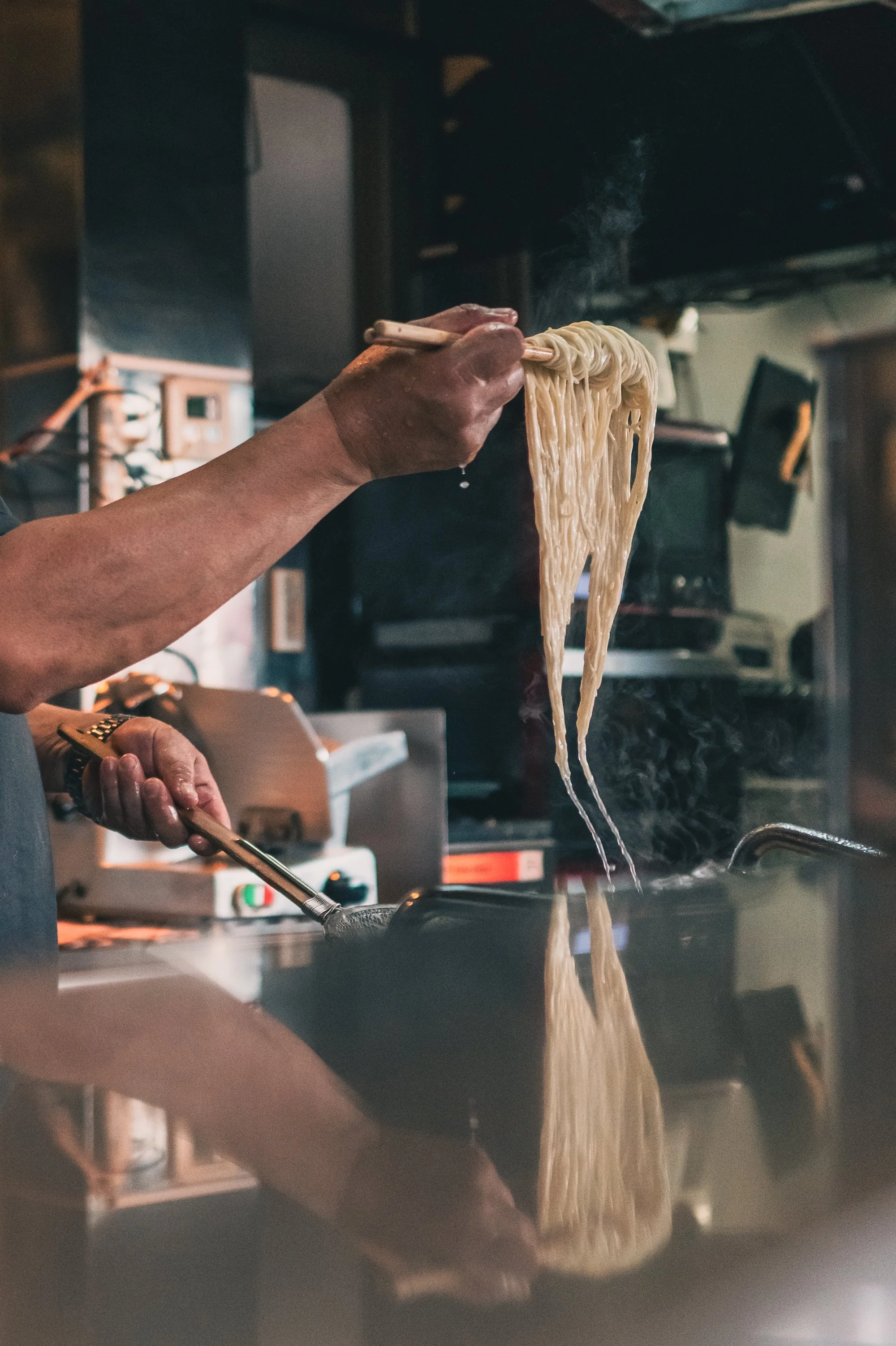 Print AD-0044. Hands lifting steaming noodles above a cooking pot.